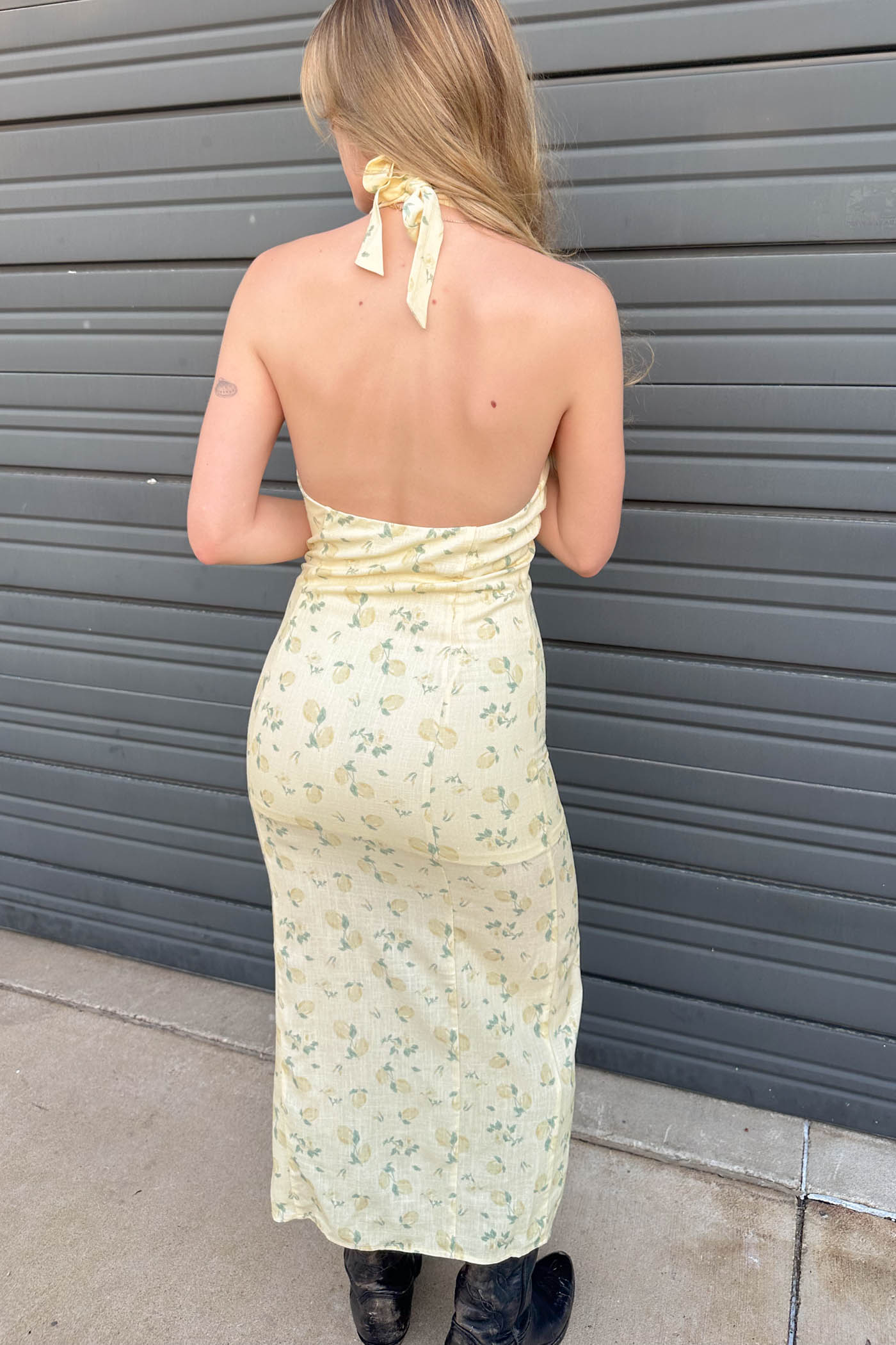 Woman wearing a floral dress standing against a gray wall.