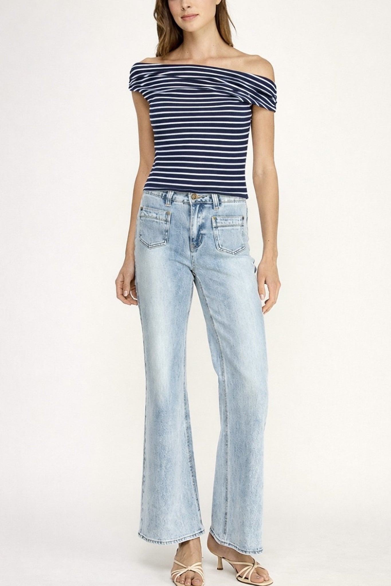 Woman wearing a striped off-shoulder top and light blue jeans on a white background