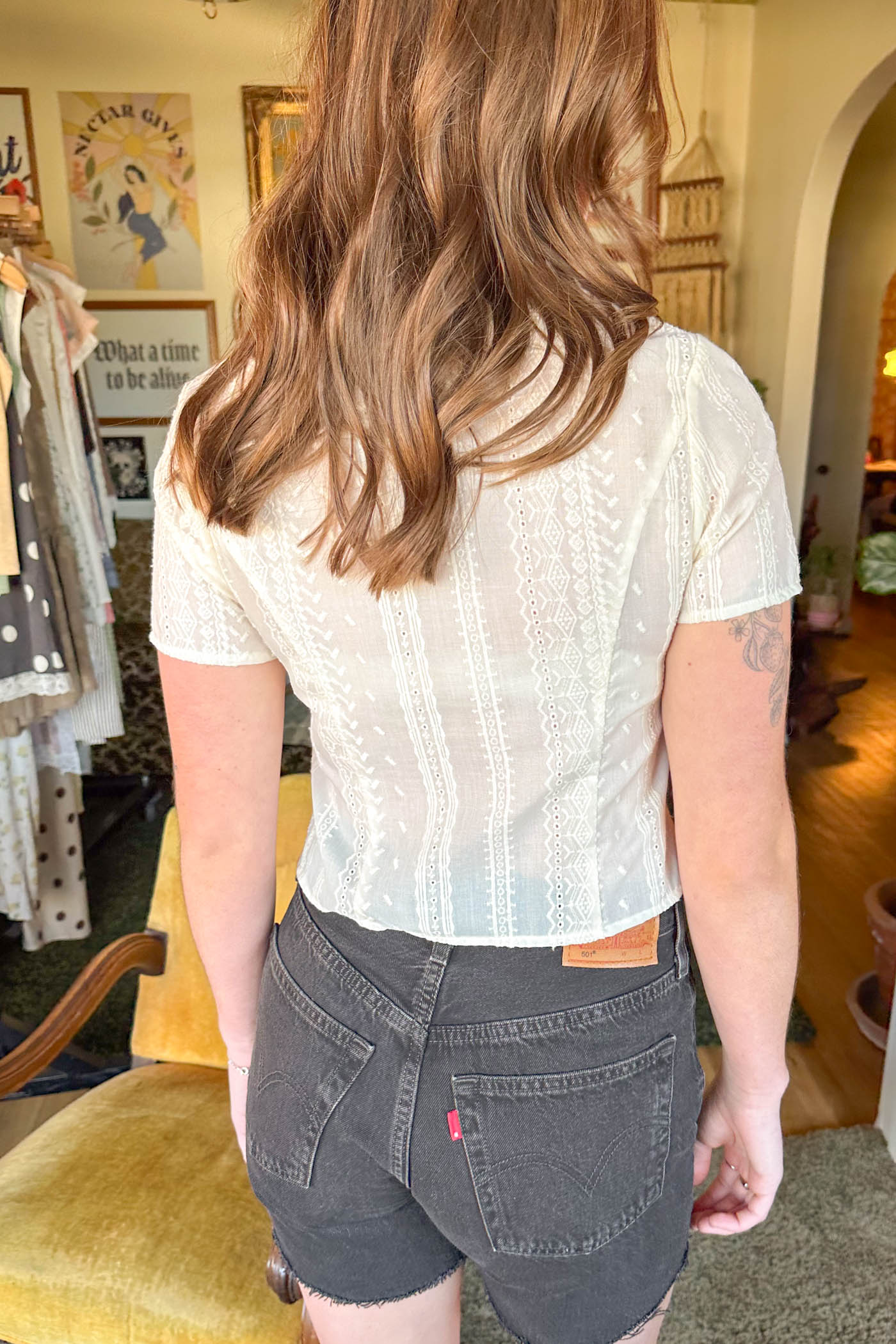 Person wearing a white blouse and dark shorts in an indoor setting with posters on the wall.