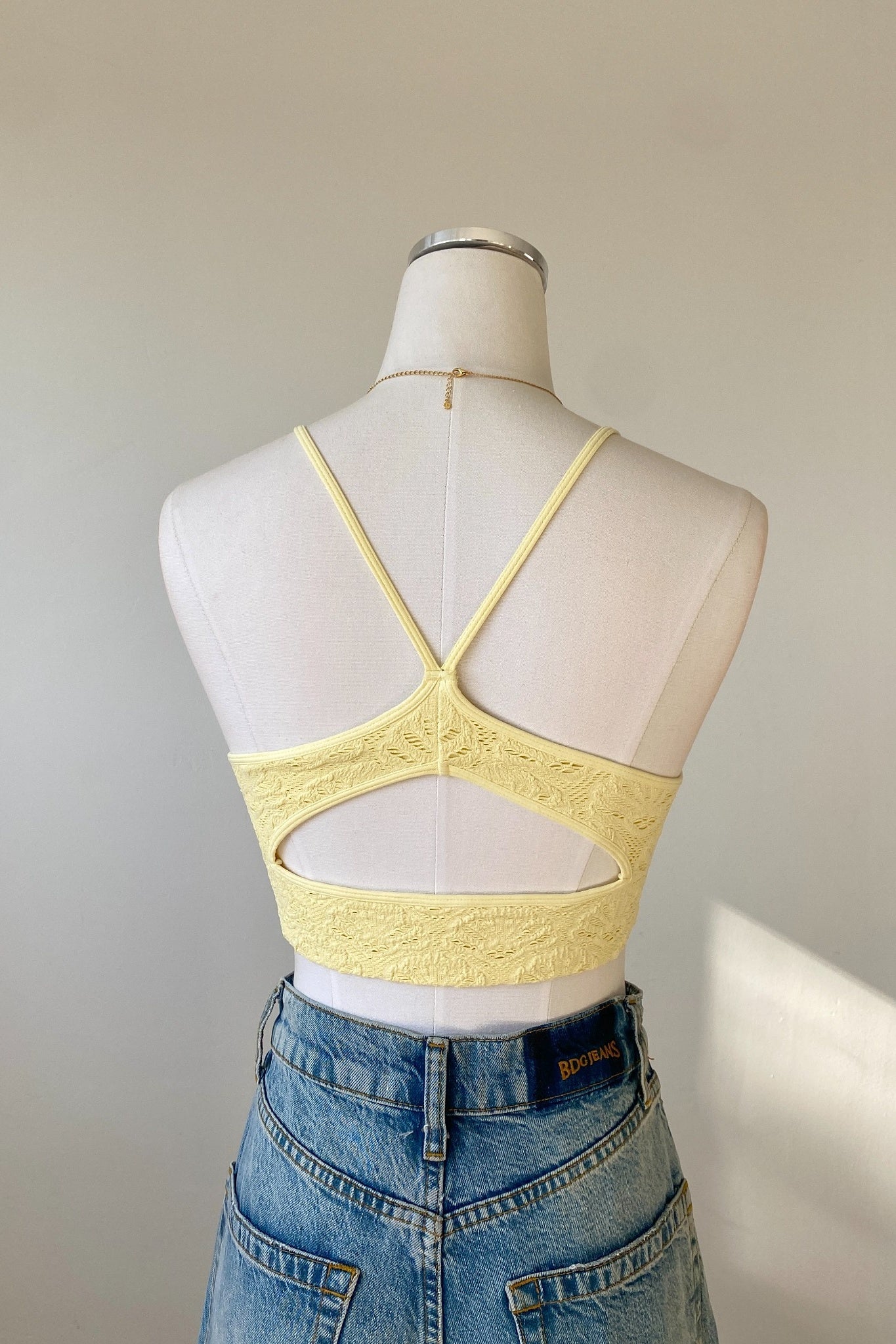 Yellow lace crop top on a mannequin with a plain background