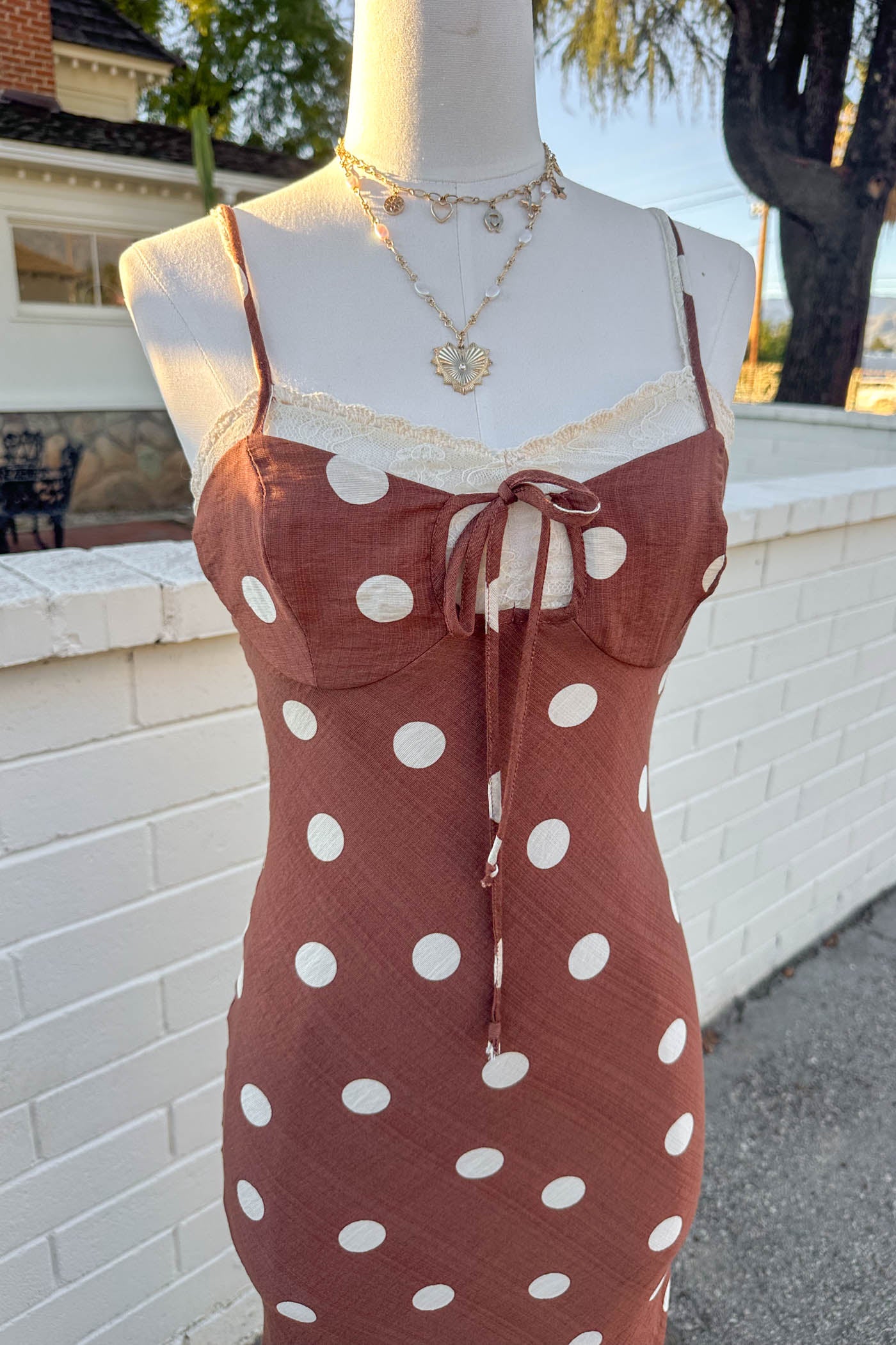 Mannequin wearing a Brown Polka Dotted Maxi Dress standing in front of a brick wall. 