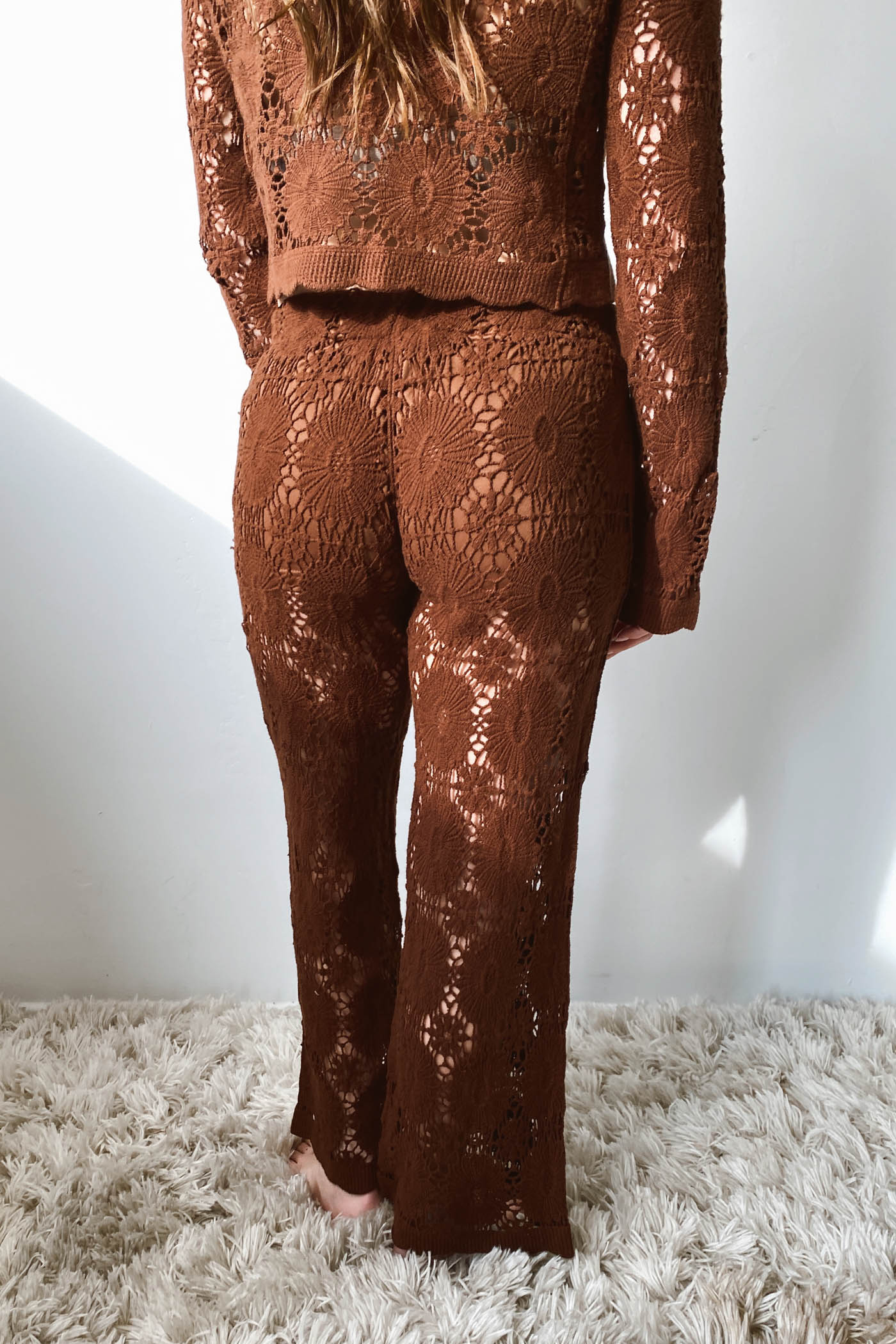 Brown lace outfit on a person standing on a textured surface with a white wall background