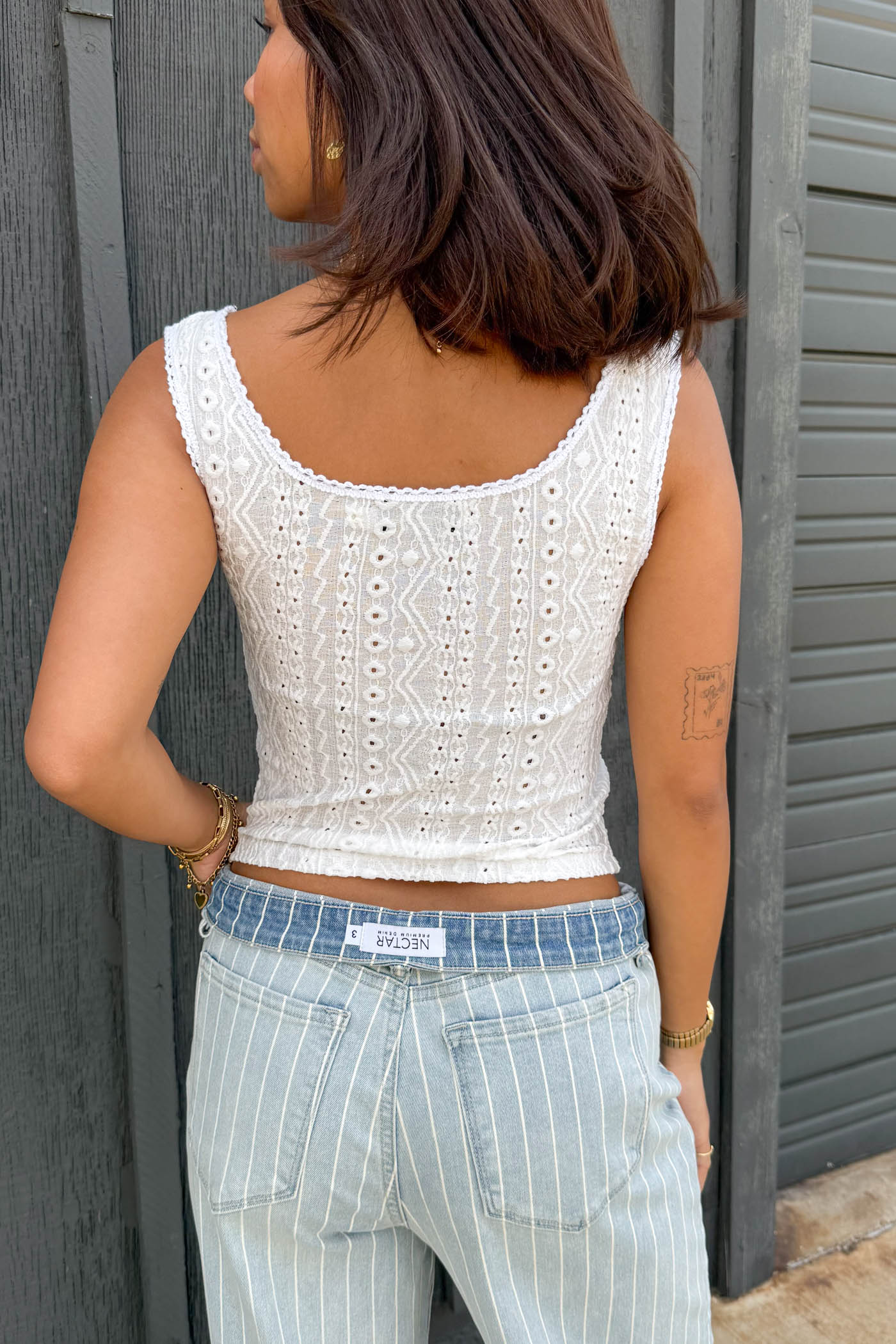 Person wearing a white sleeveless top and striped pants against a gray wall.