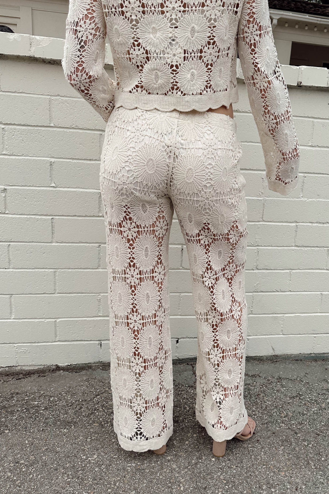 Person wearing a matching lace outfit against a white brick wall.
