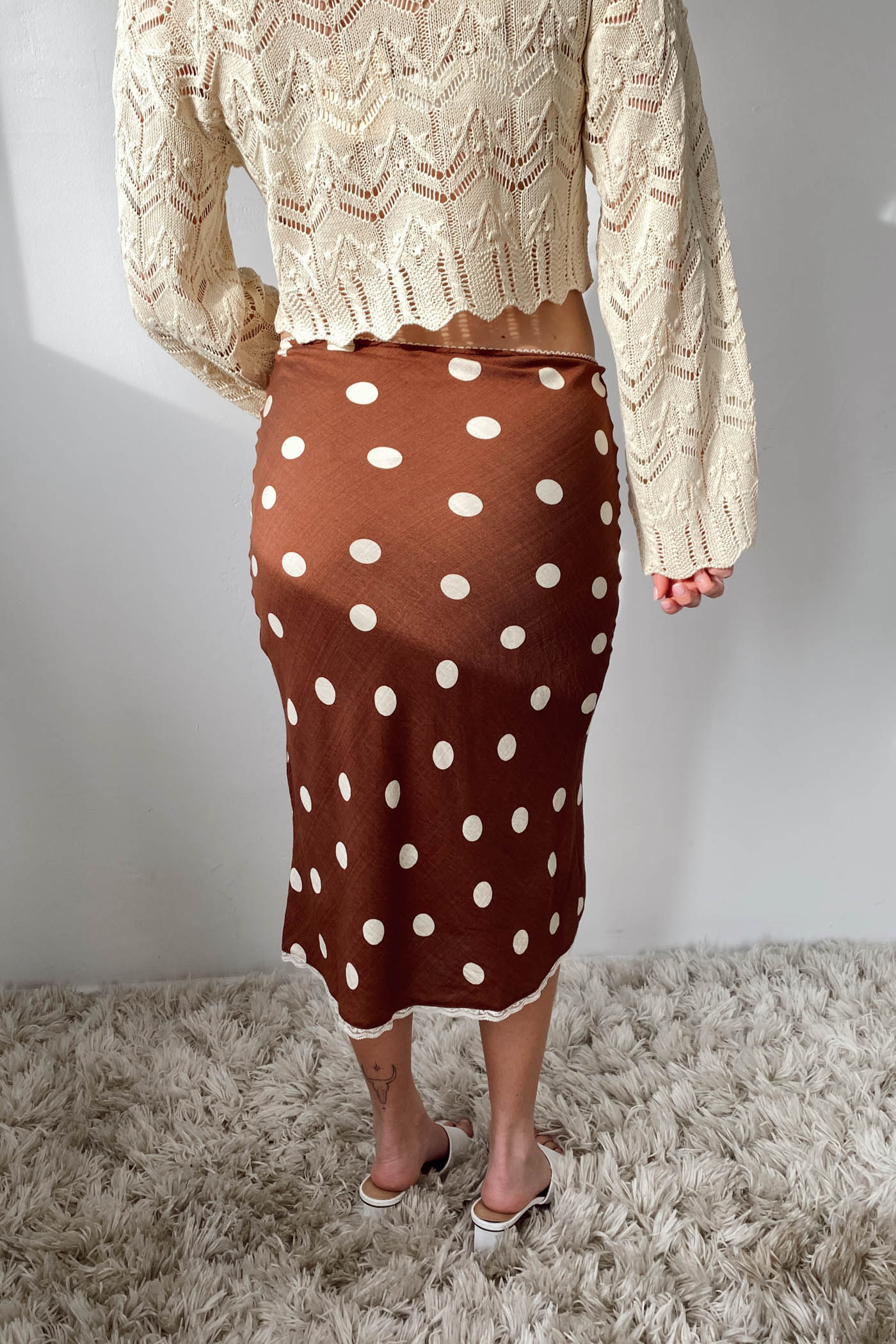 Person wearing a beige lace top and brown polka dot skirt on a neutral background