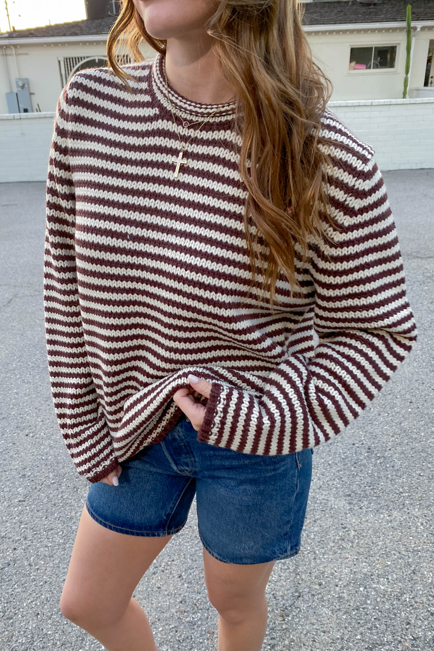 Person wearing a striped sweater and denim shorts outdoors.