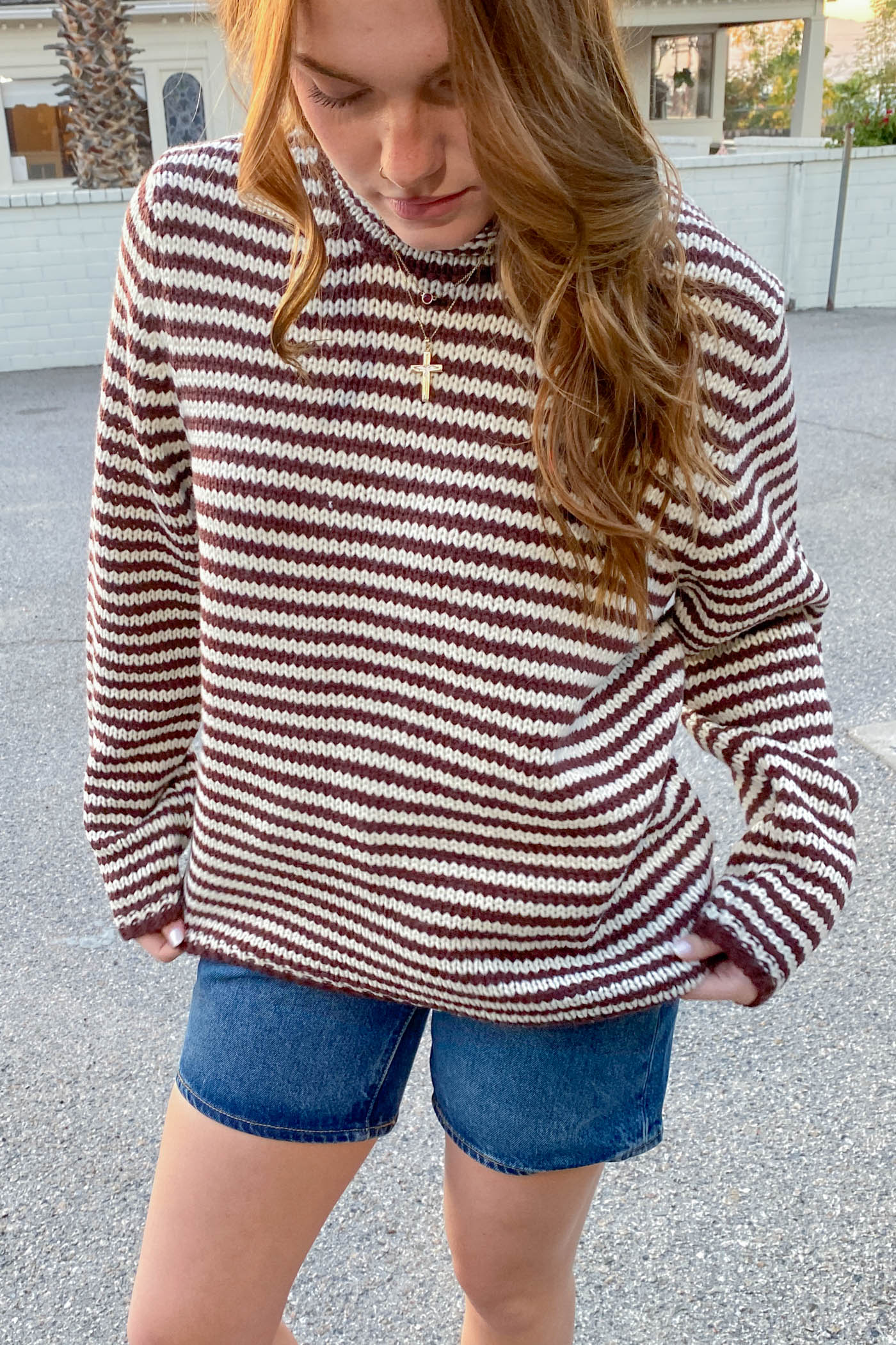 Person wearing a striped sweater and denim shorts outdoors.