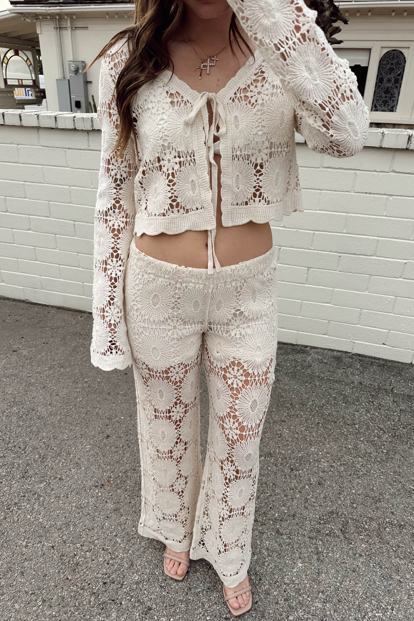 Person wearing a white lace outfit standing against a white brick wall.