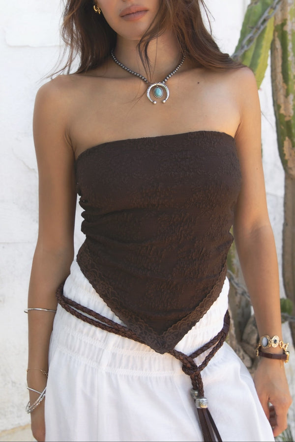 Woman wearing a strapless brown top with a white skirt against a white wall.