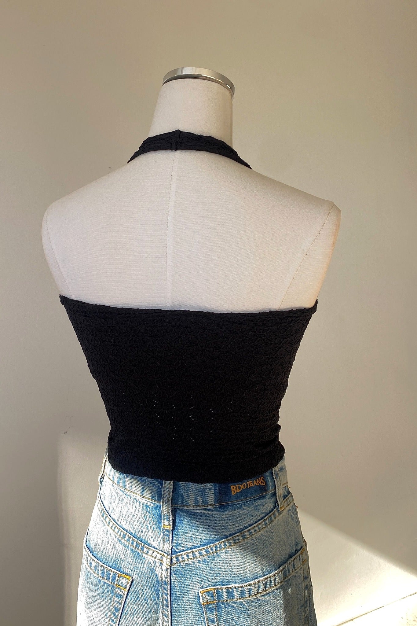 Black halter top and blue jeans on a mannequin against a neutral background
