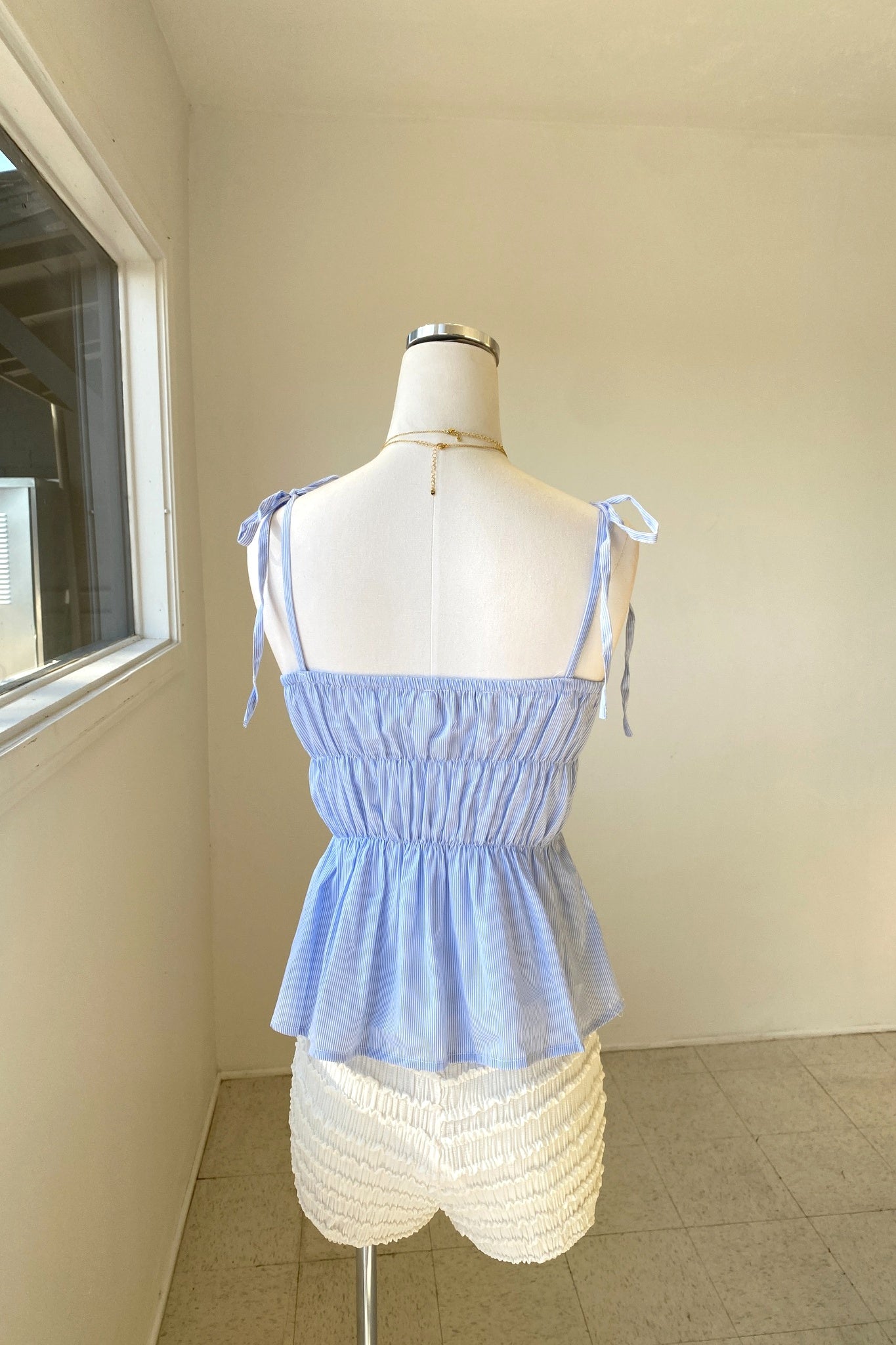 Light blue top and white shorts on a mannequin against a plain wall.