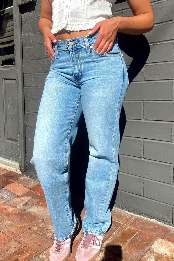 Person wearing light blue jeans and a white top against a gray wall.