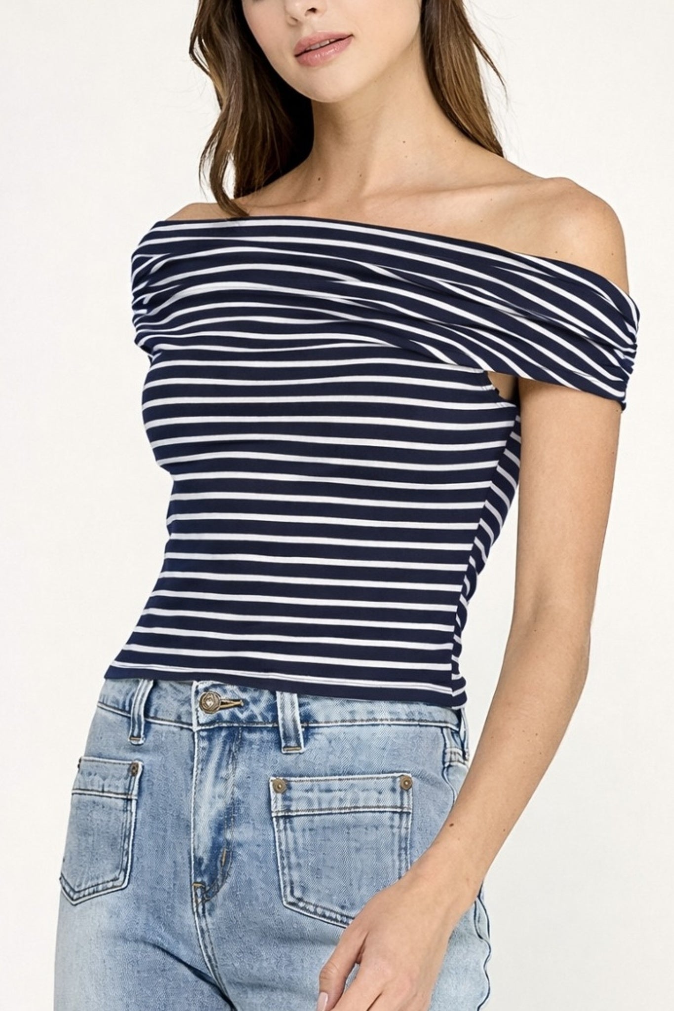 Woman wearing a navy and white striped off-shoulder top with blue jeans on a light background