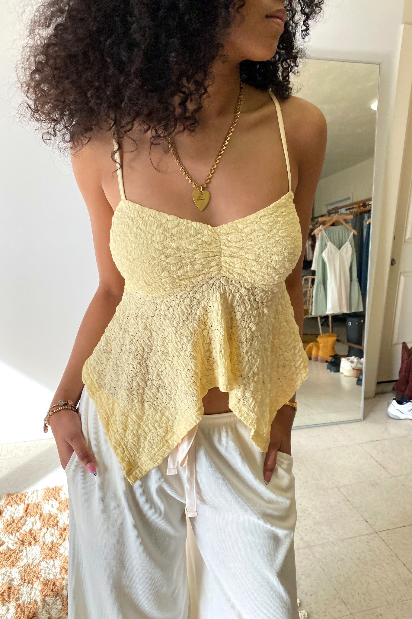 Woman wearing a yellow top and white pants in a room with a mirror.