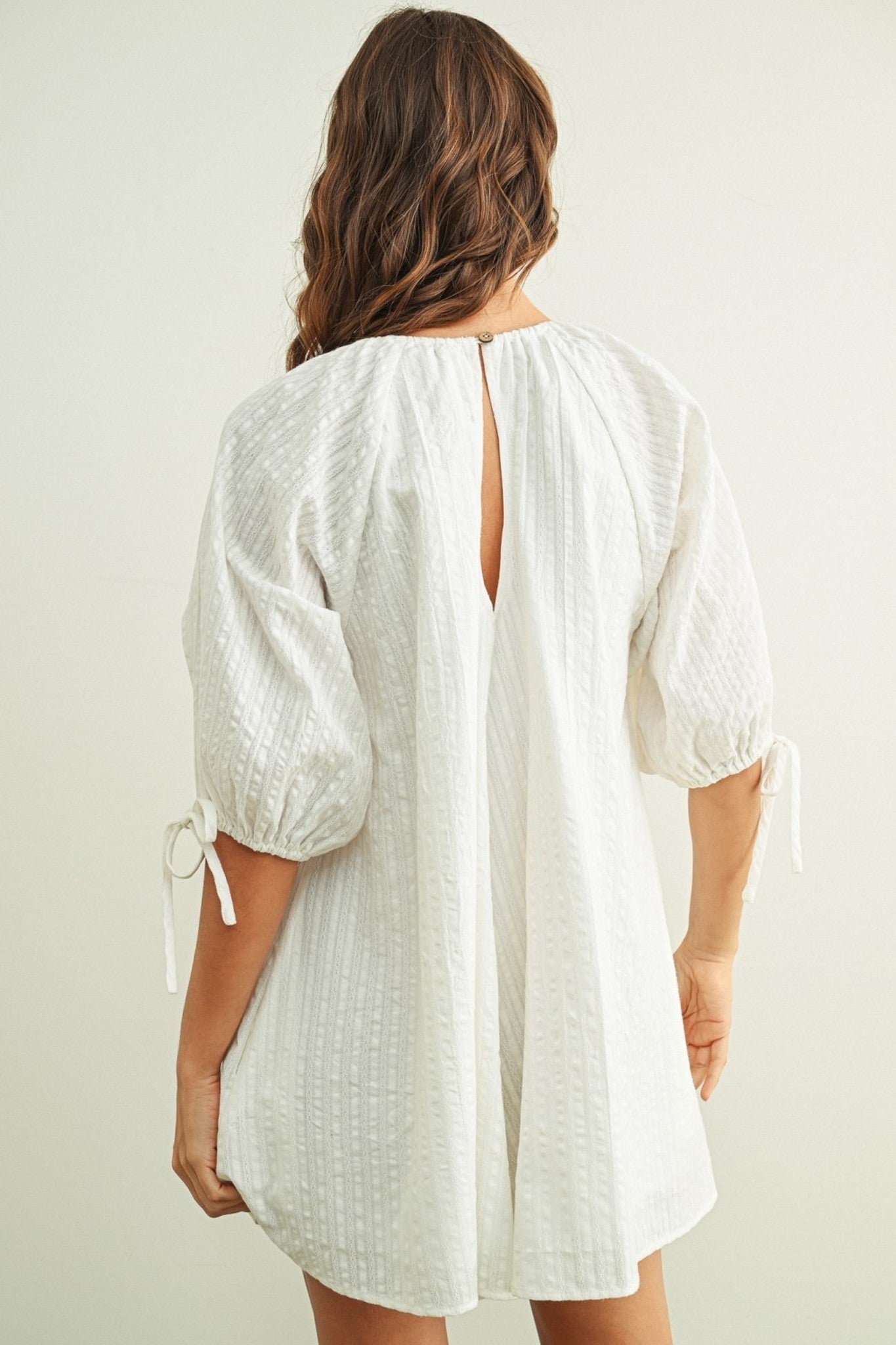 Woman wearing a white dress with a backless design on a plain background