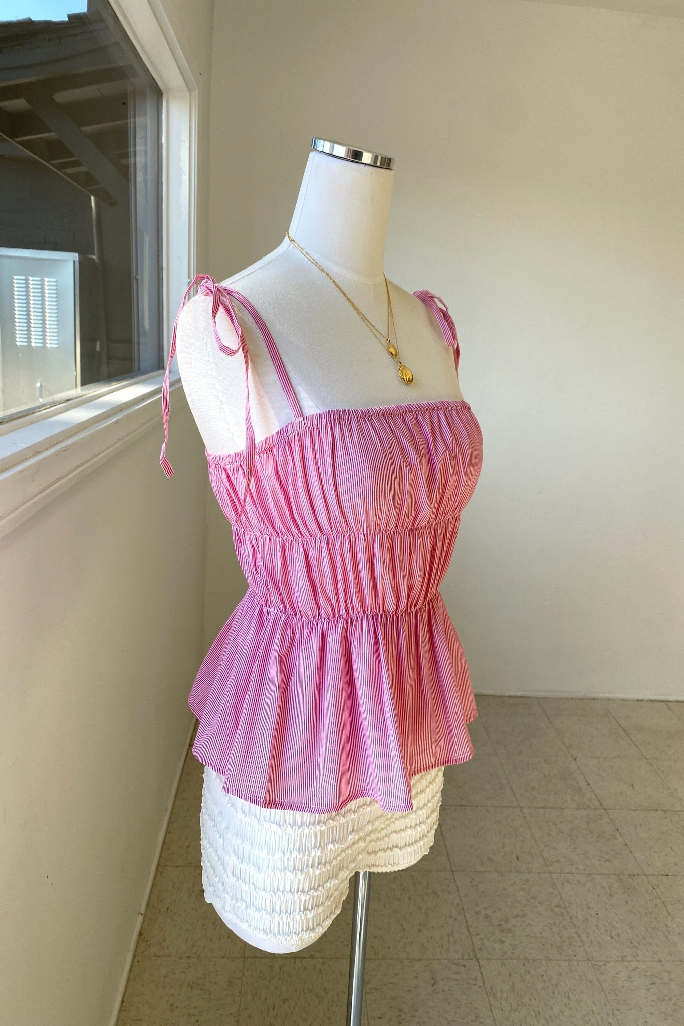 Mannequin wearing a pink top and white skirt against a neutral wall.