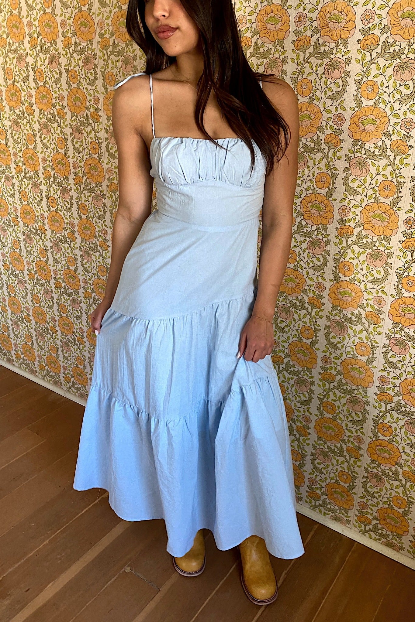 Woman wearing a light blue dress with floral wallpaper in the background