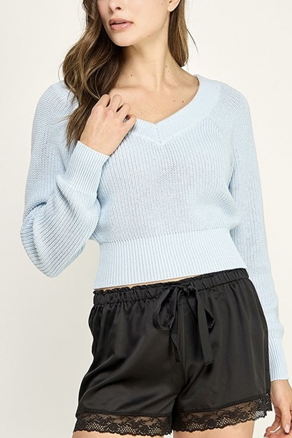 Woman wearing a light blue sweater and black shorts with lace trim on a beige background