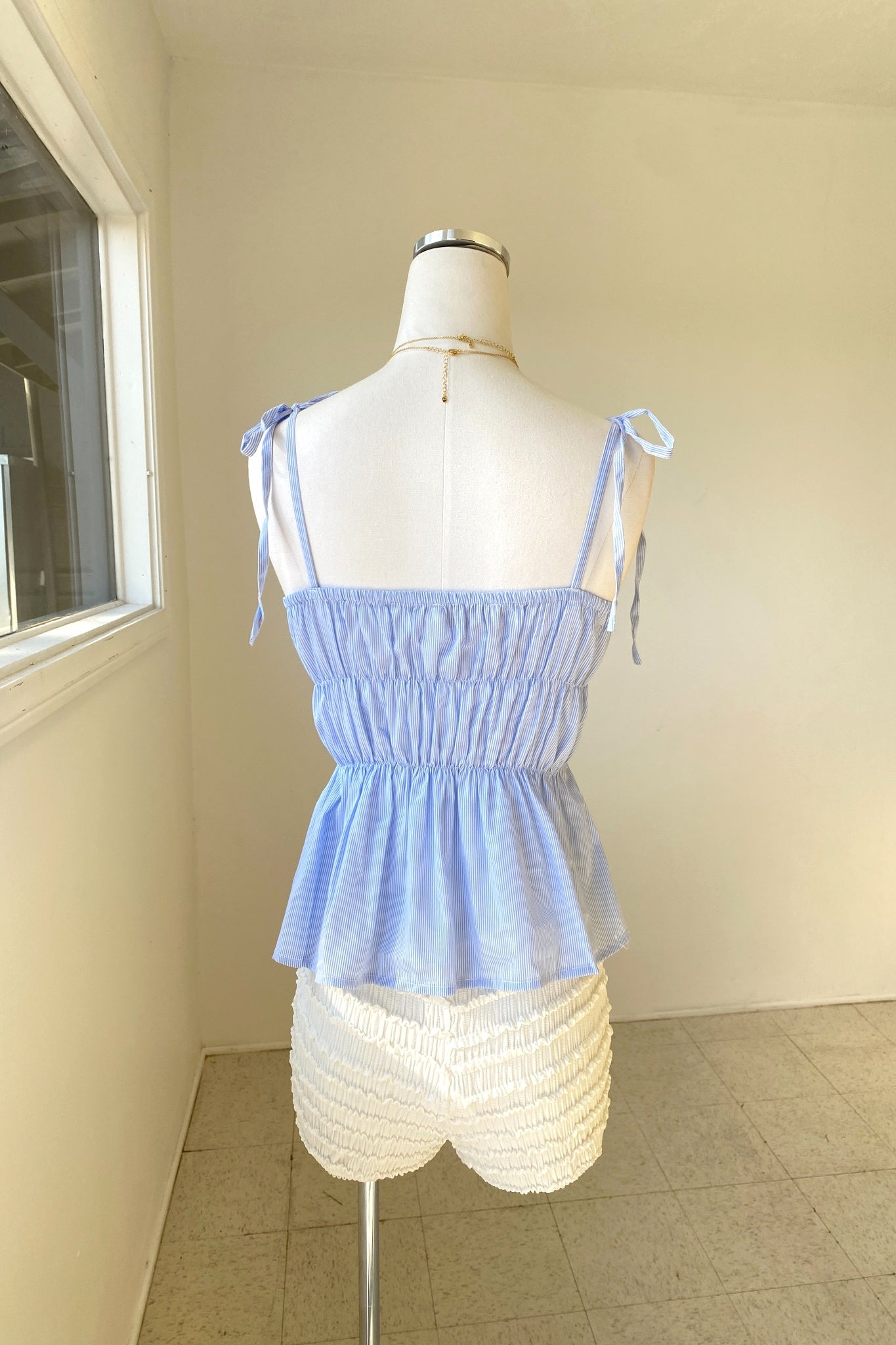 Light blue top on a mannequin against a neutral wall.