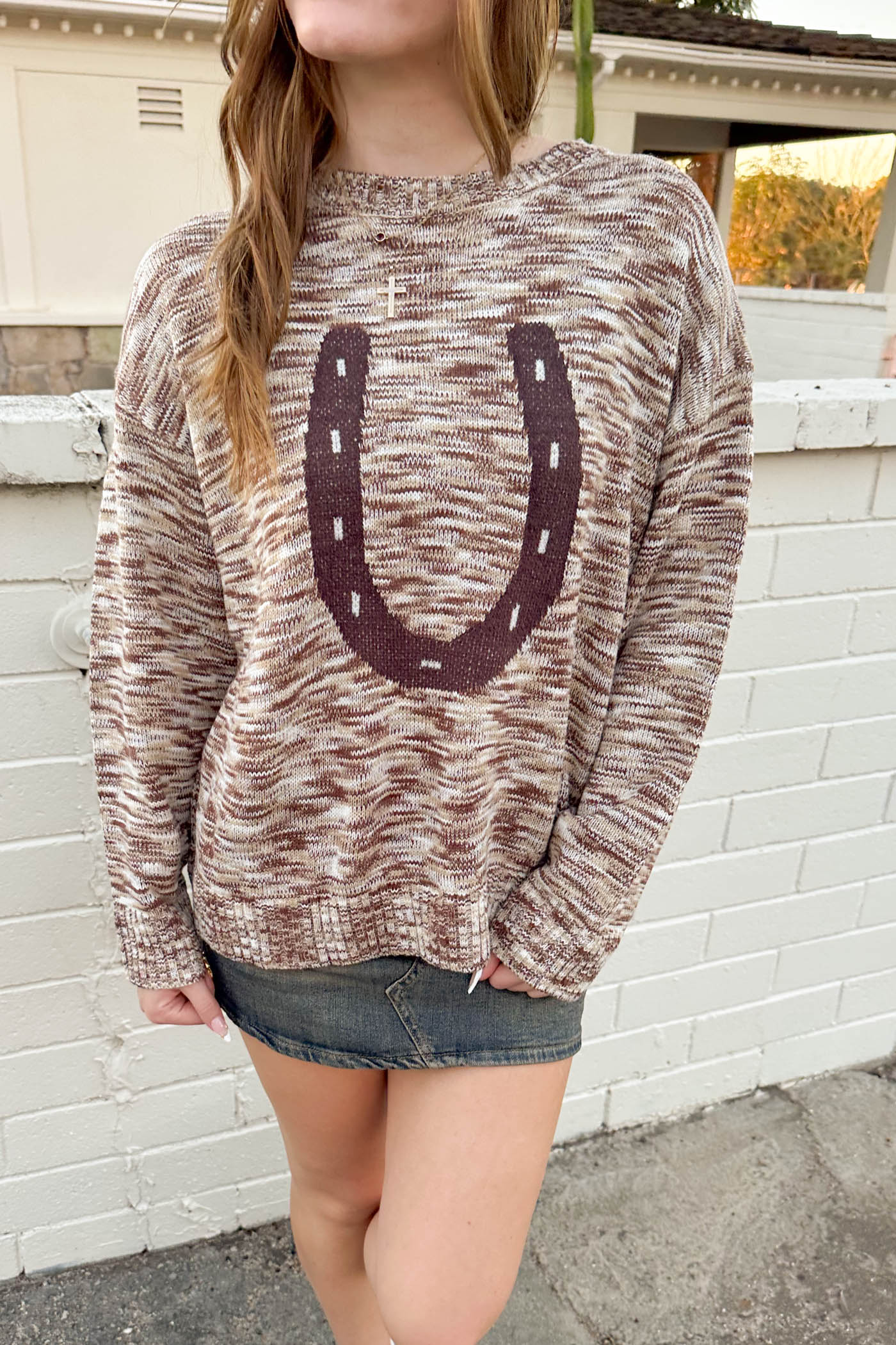 Person wearing a patterned sweater with a large 'U' design in front of a white brick wall.