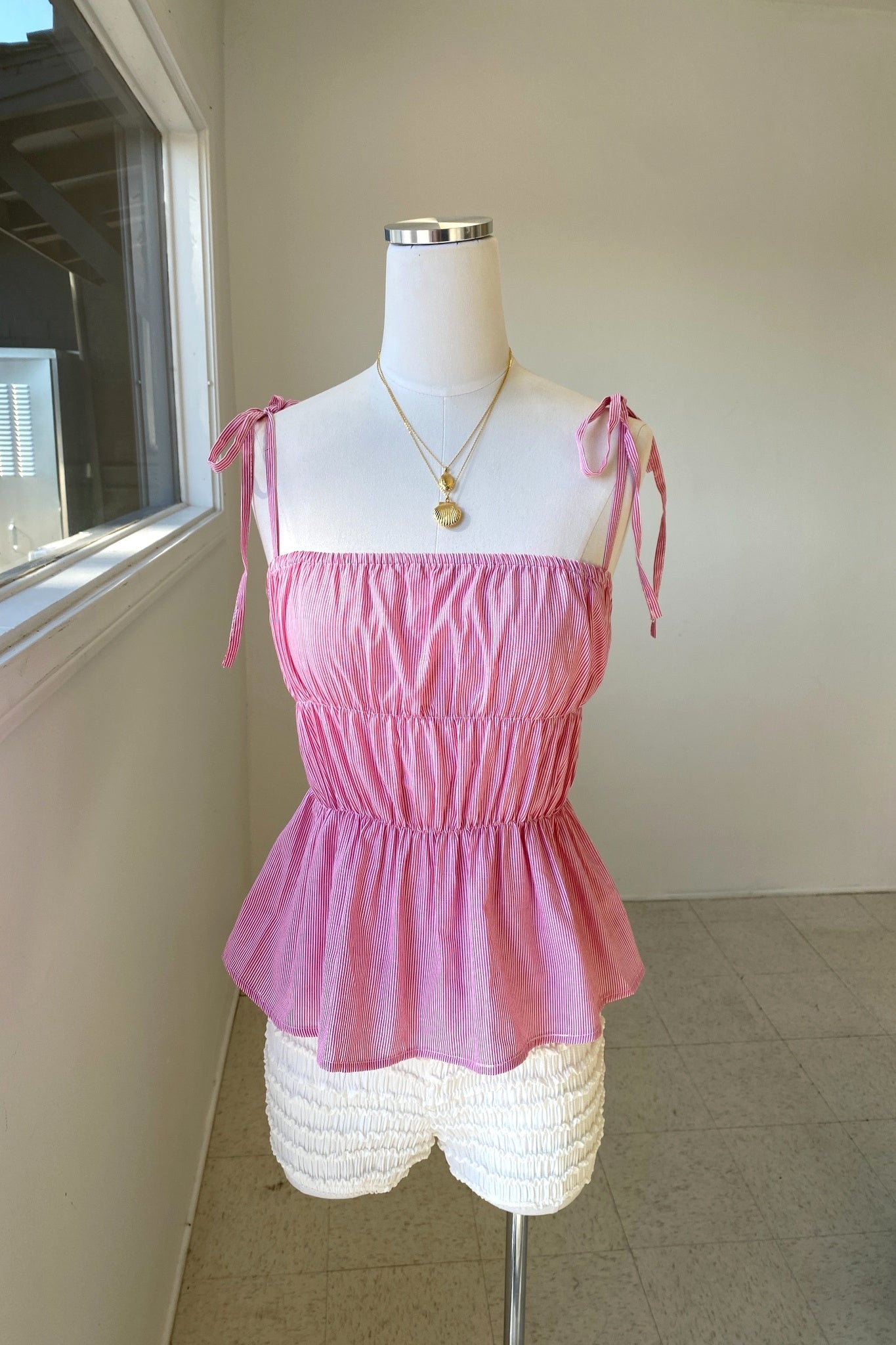 Mannequin wearing a pink top and white shorts against a neutral wall.