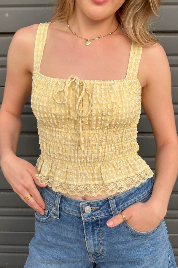 Person wearing a yellow textured top and blue jeans against a gray background