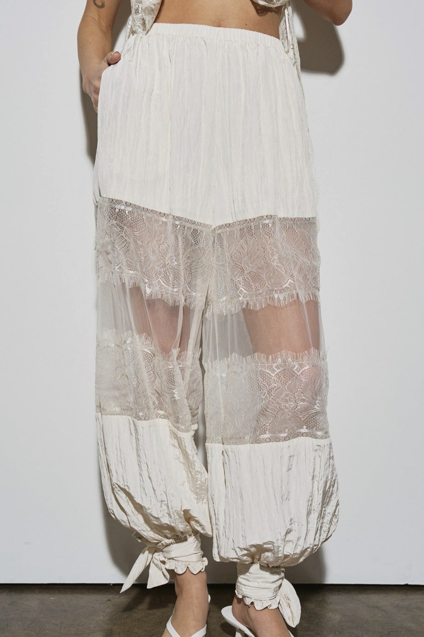 White lace-trimmed pants with sheer panels on a plain background