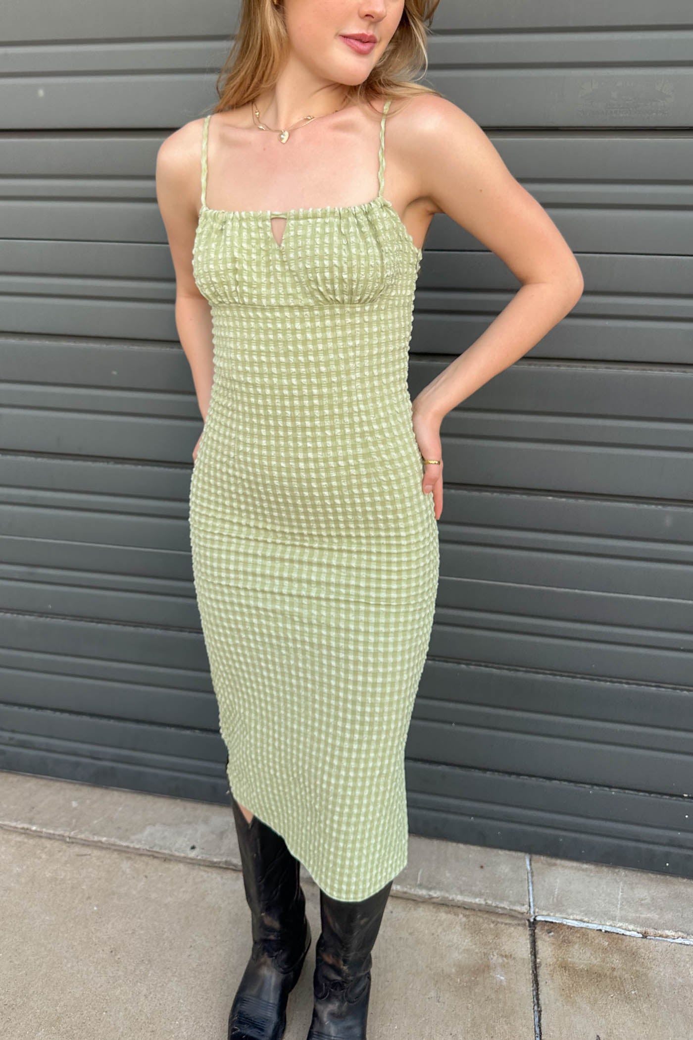 Woman wearing a green checkered dress standing against a gray wall.