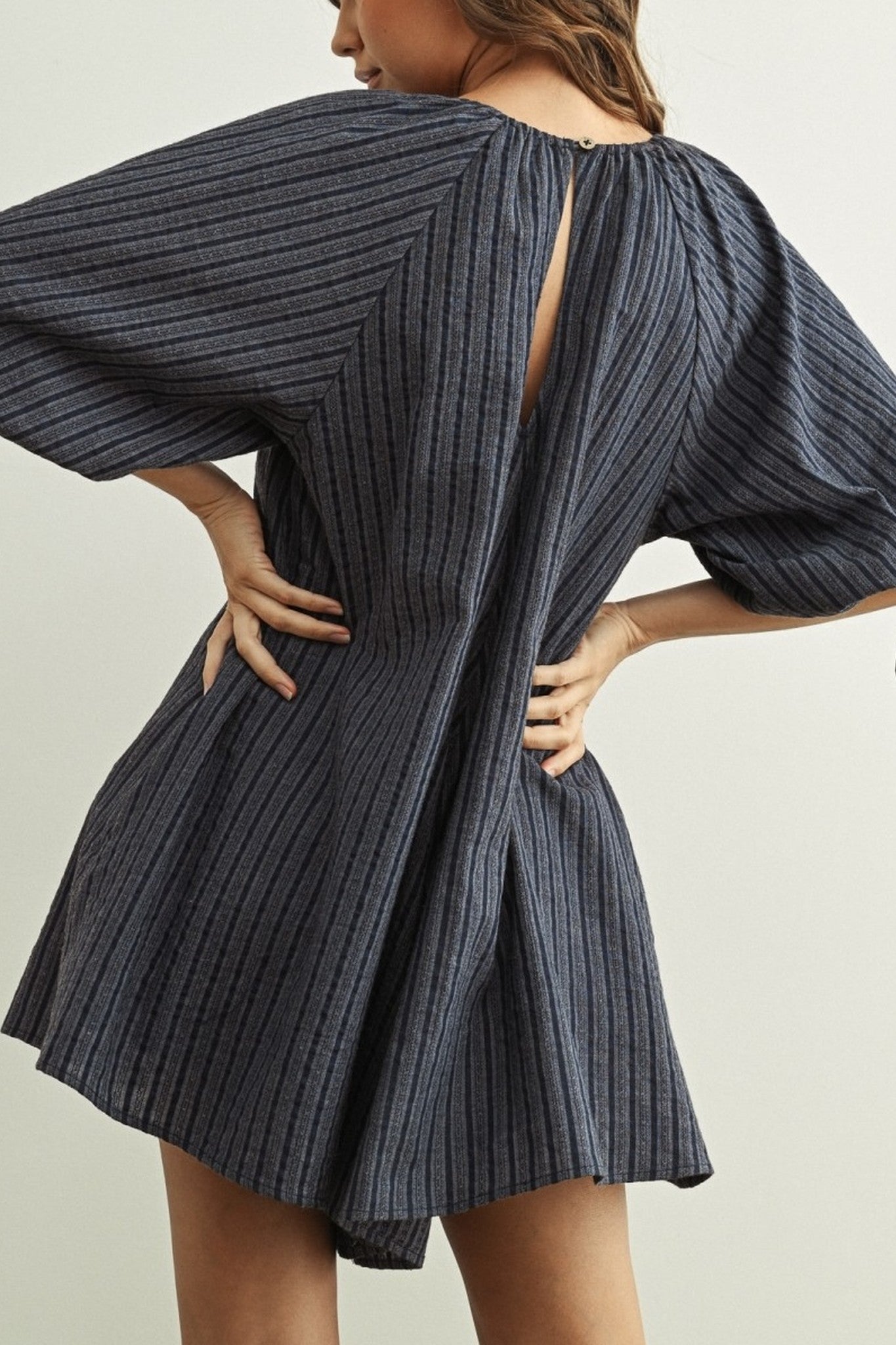 Woman wearing a dark blue ribbed dress with puffed sleeves on a light background