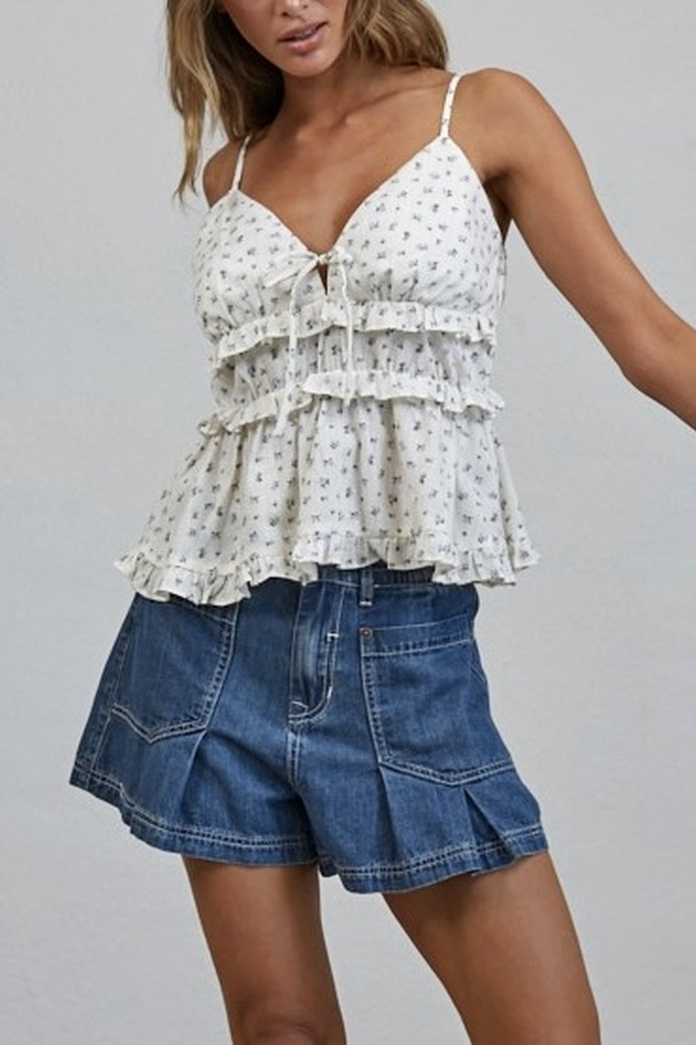 Woman wearing a white floral top and blue denim shorts on a gray background