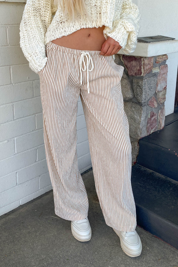 Person wearing a white knit sweater and striped pants standing against a brick wall.