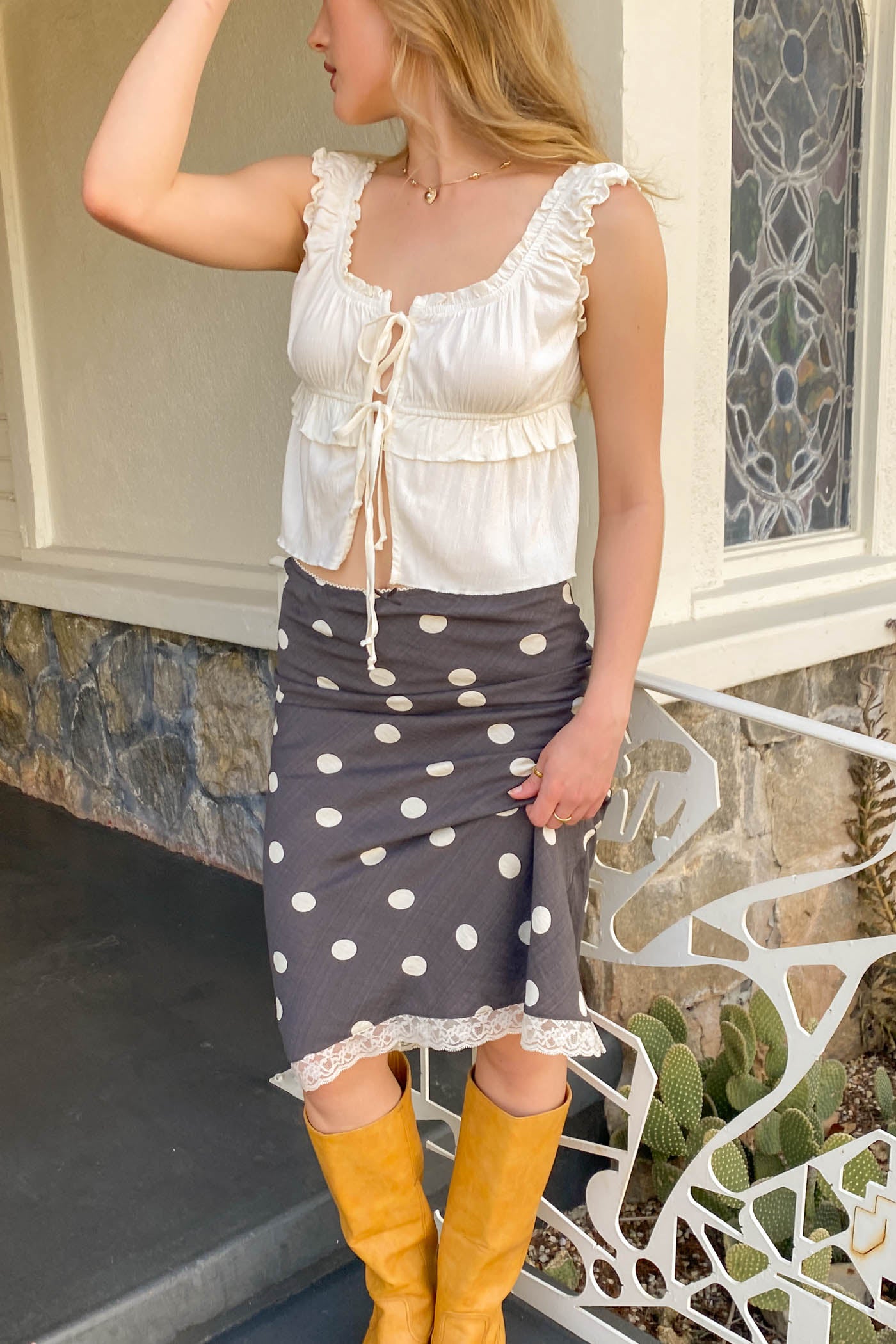 Woman wearing a white blouse with ruffles and a gray skirt with white polka dots, standing outdoors.
