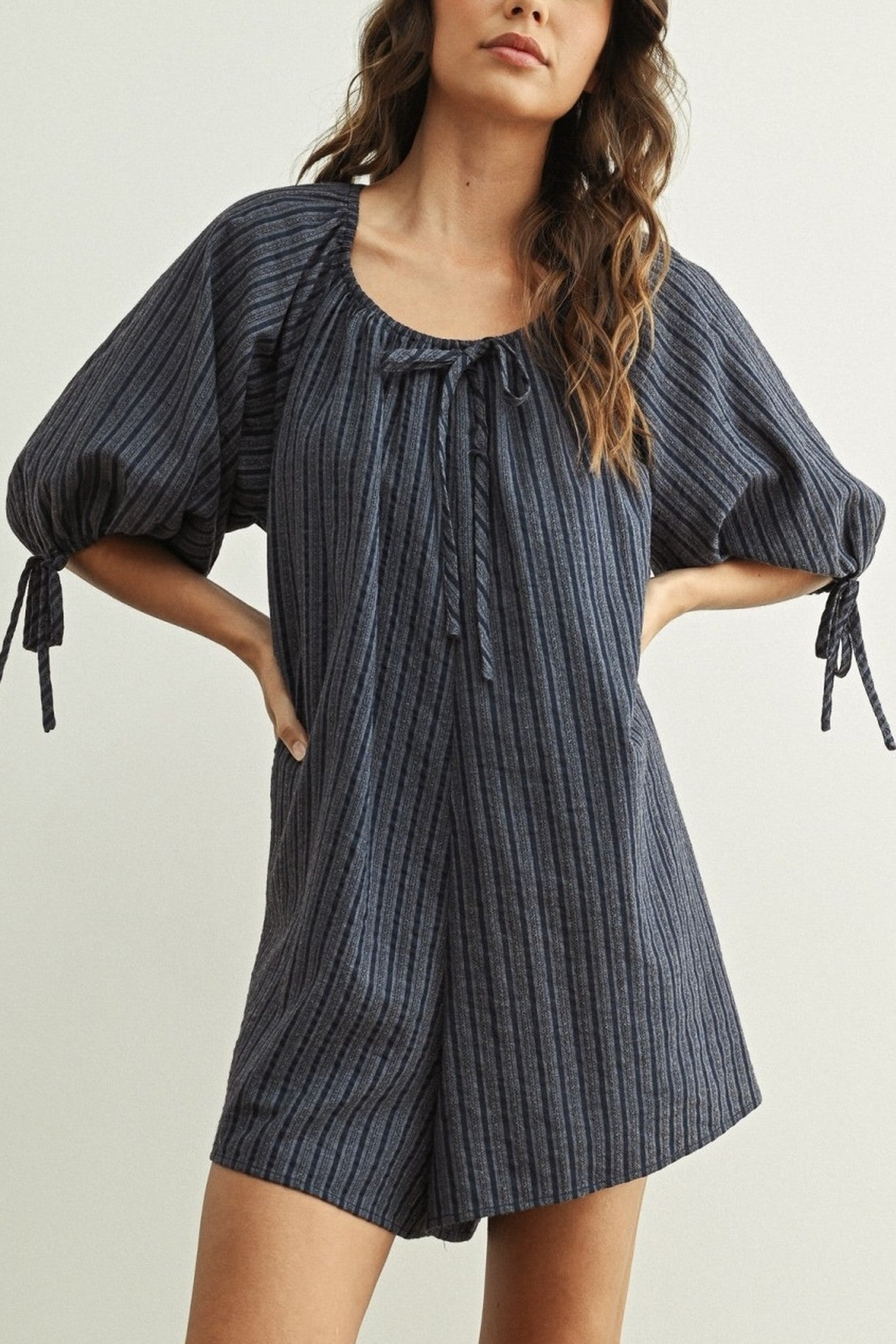 Woman wearing a blue striped romper with puff sleeves on a plain background