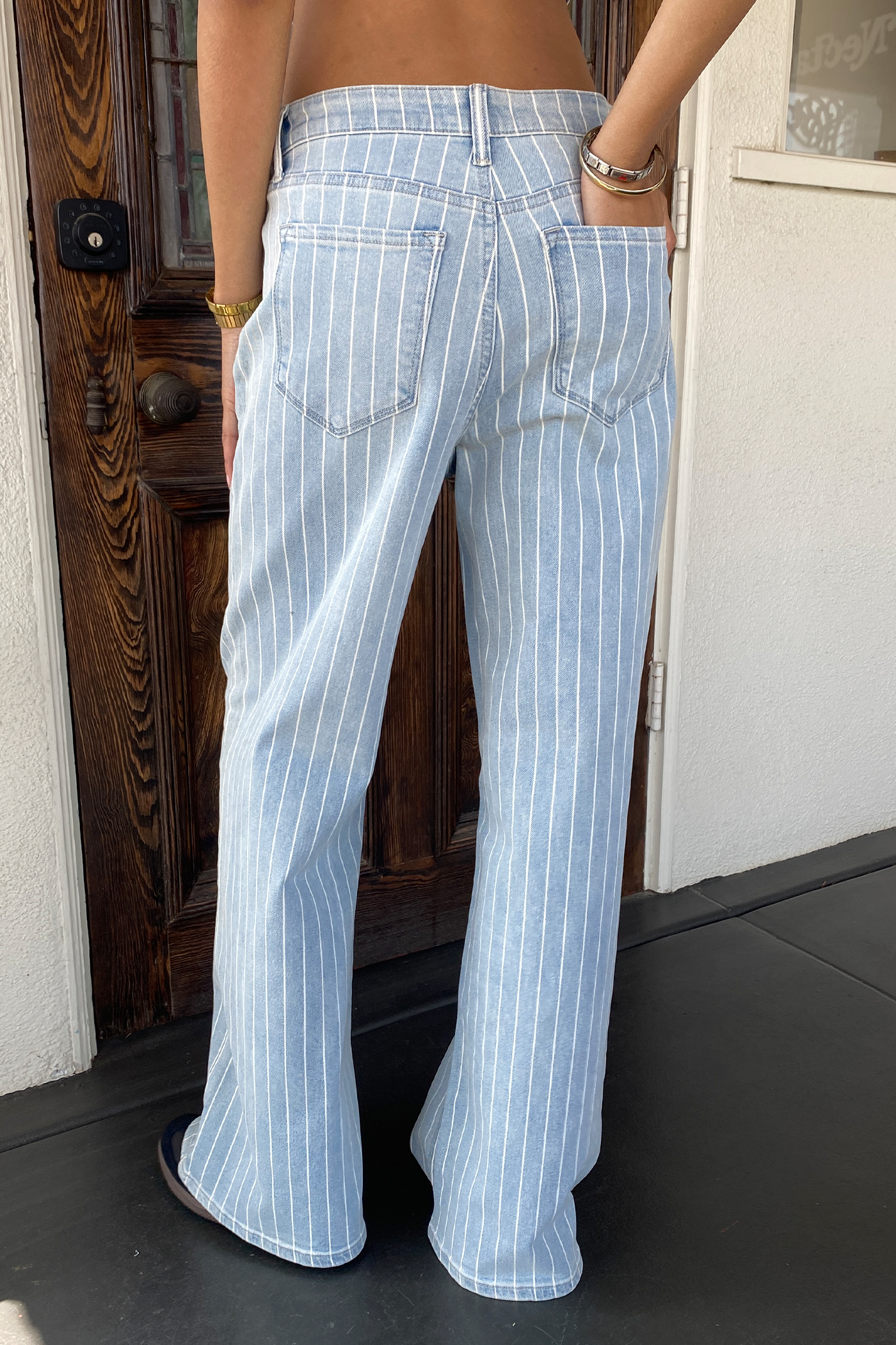 Person wearing light blue pinstripe pants standing in front of a wooden door.