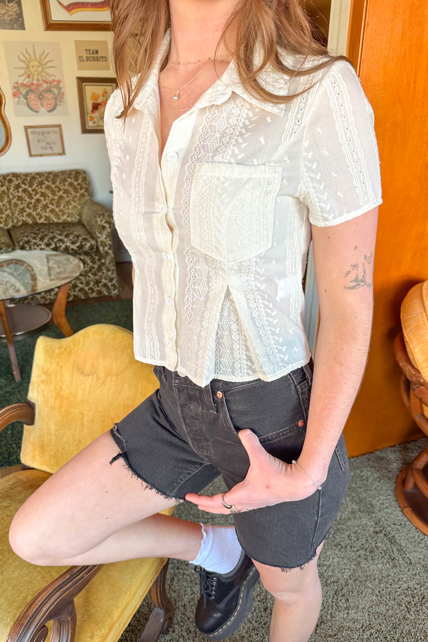 Person wearing a white lace blouse and black shorts in an indoor setting.