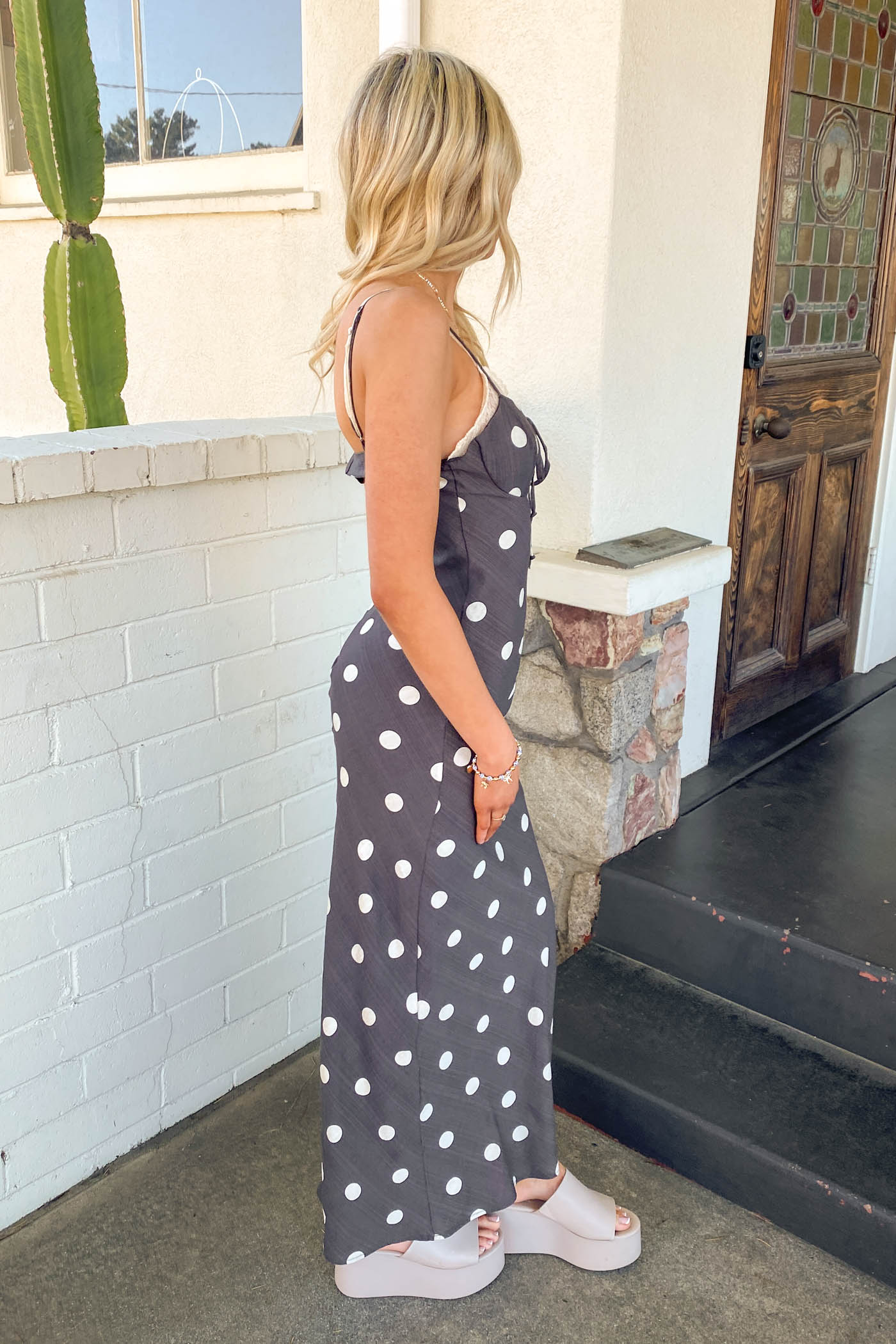 Girl wearing a black Polka Dotted Maxi Dress standing in front of a brick wall. 
