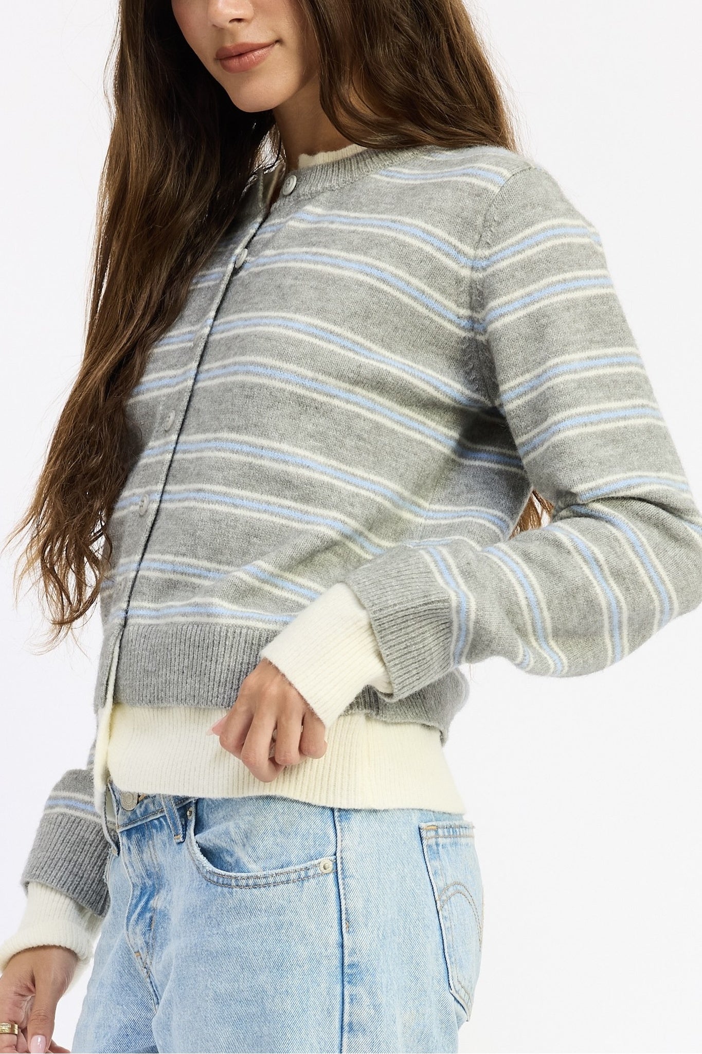 A woman wearing a gray knit zip-up cardigan with thin light blue and white horizontal stripes, paired with light-wash blue jeans against a plain white background.