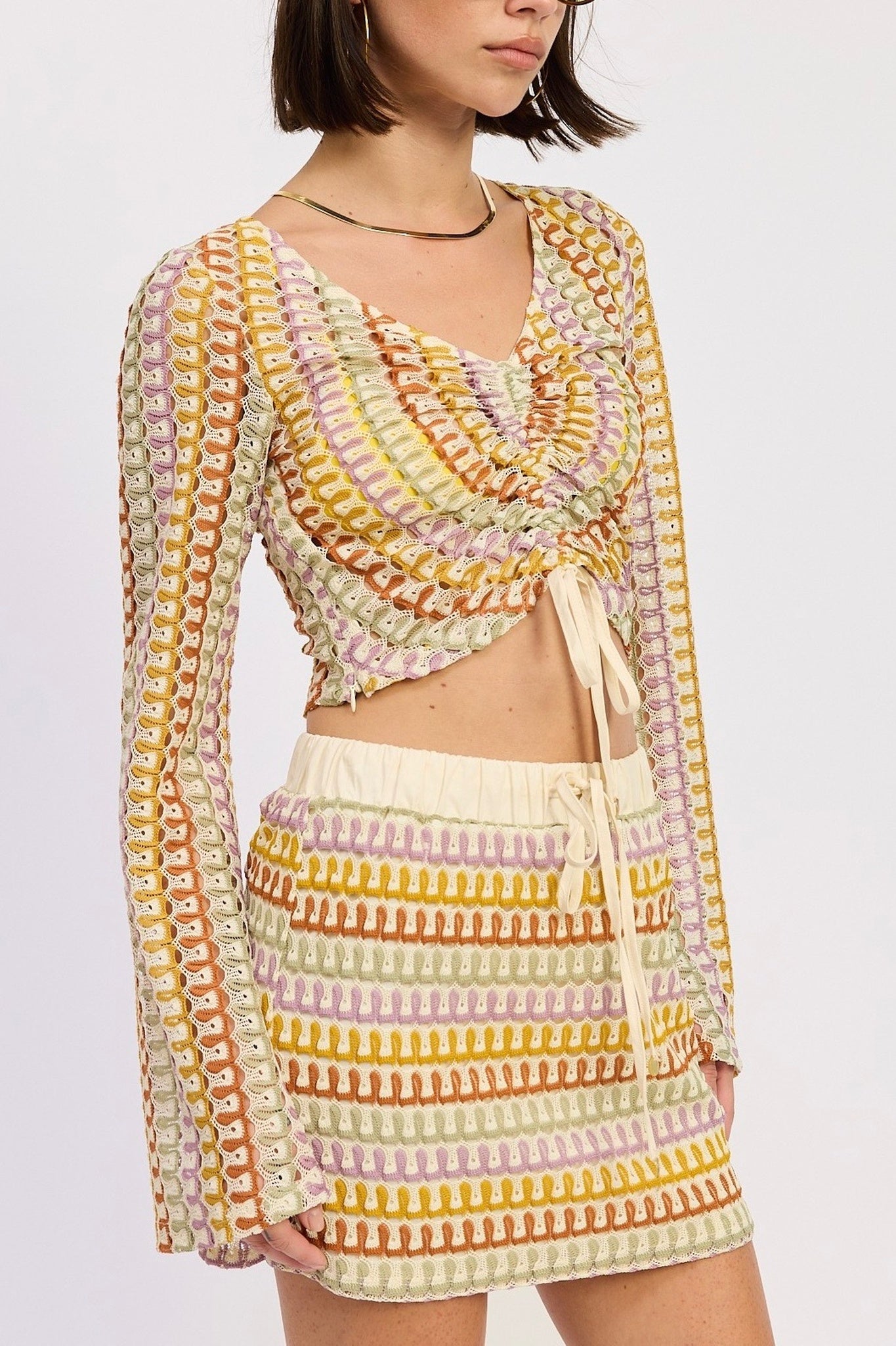 Woman wearing a colorful crochet outfit with a patterned cardigan and skirt on a white background