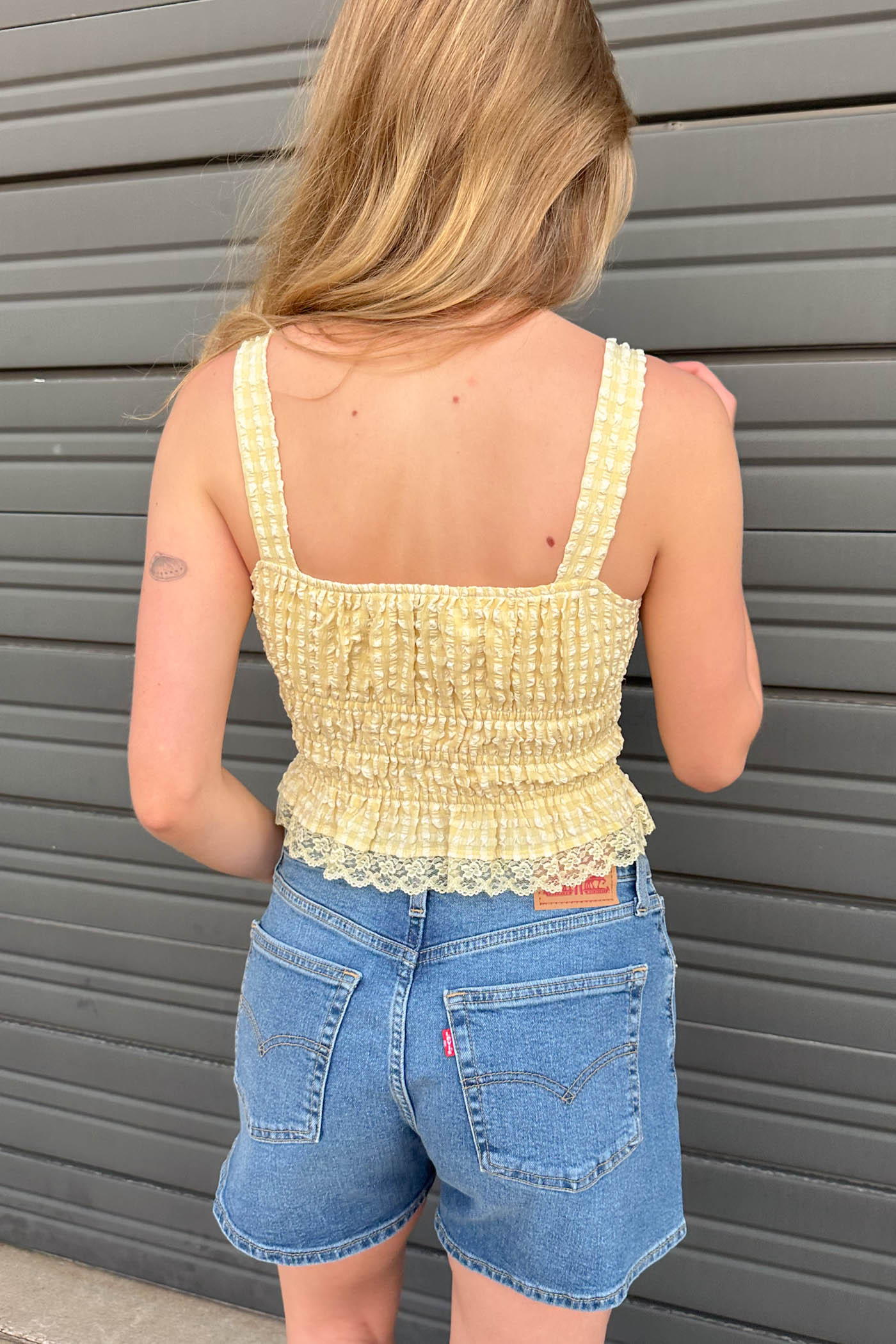 Person wearing a yellow top and blue shorts standing against a gray metallic background