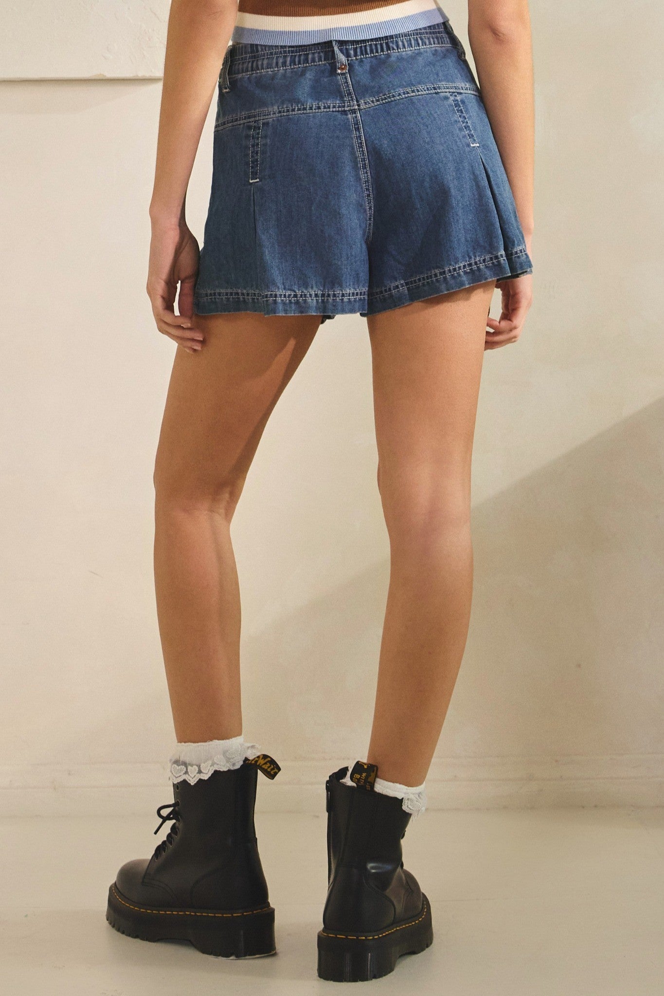 Person wearing a blue denim skirt and black boots on a plain background