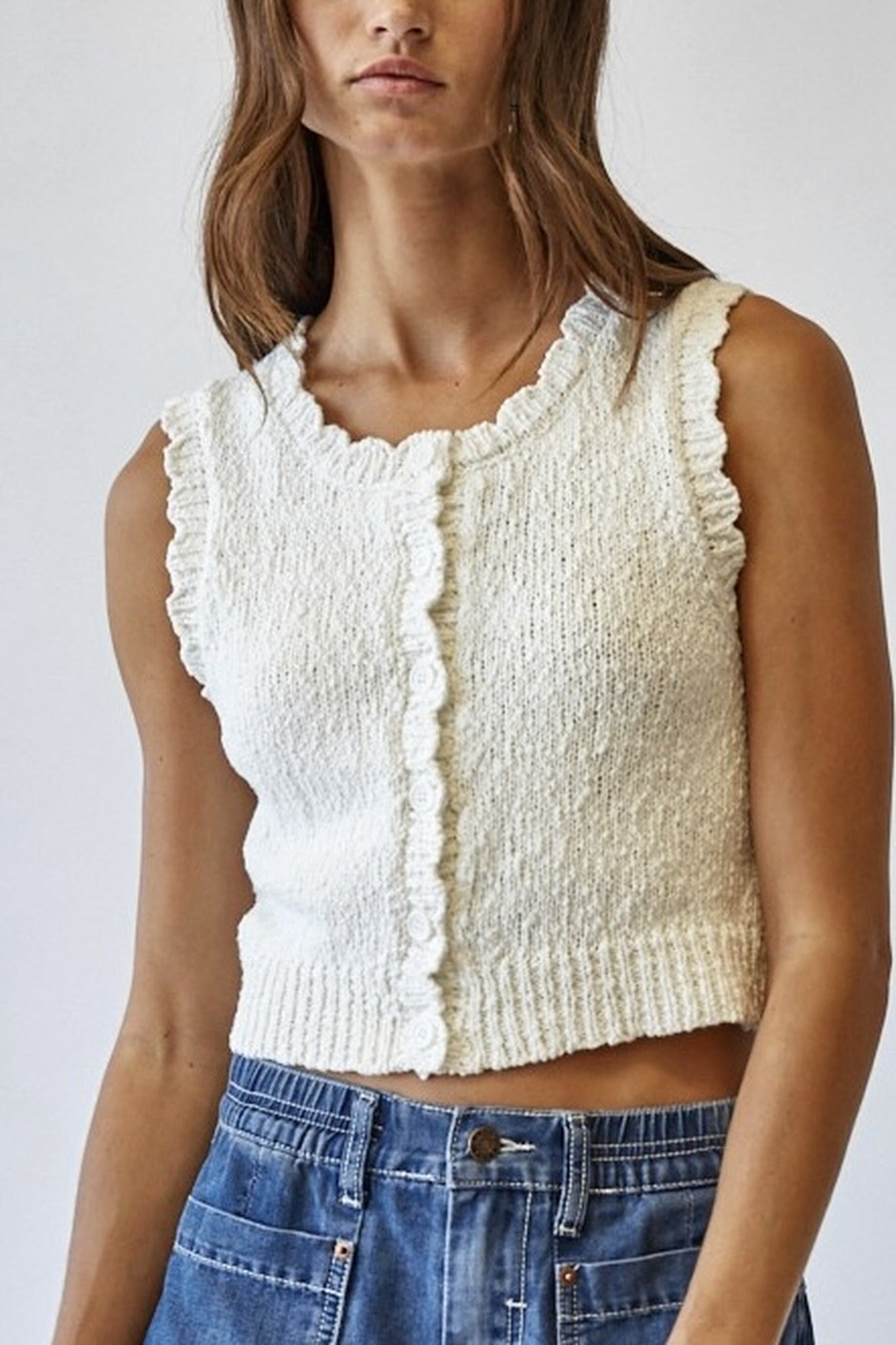 Woman wearing a textured white sleeveless top and blue jeans against a plain background