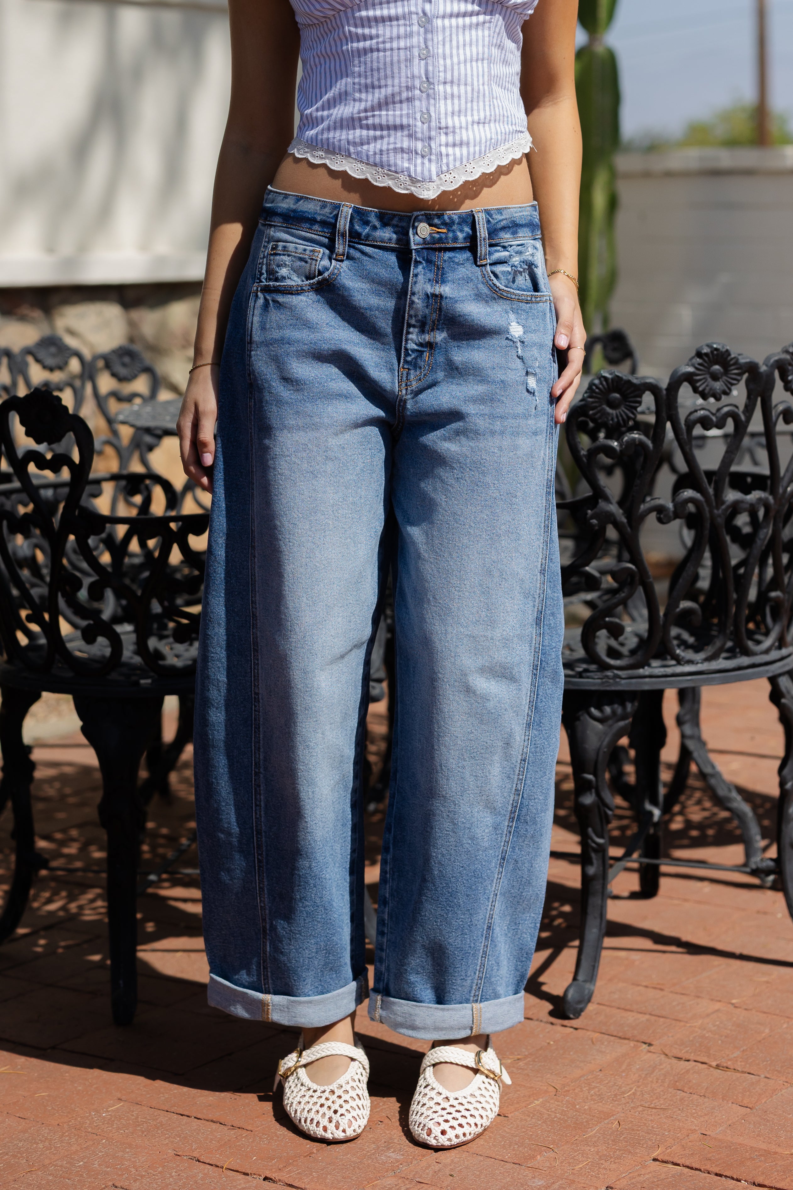Person wearing blue jeans and a white top standing outdoors on a patio.