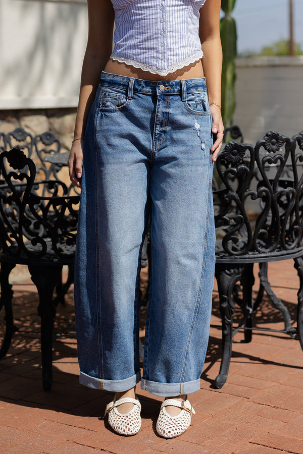 Person wearing blue jeans and a white top standing outdoors on a patio.