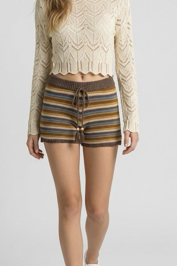 Person wearing a beige knit sweater and striped shorts on a plain background