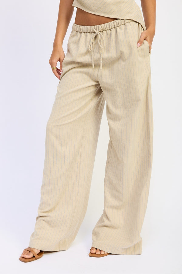 A person wearing loose, wide-leg drawstring pants in a light beige or cream color, paired with a matching top and sandals, photographed against a plain light background.