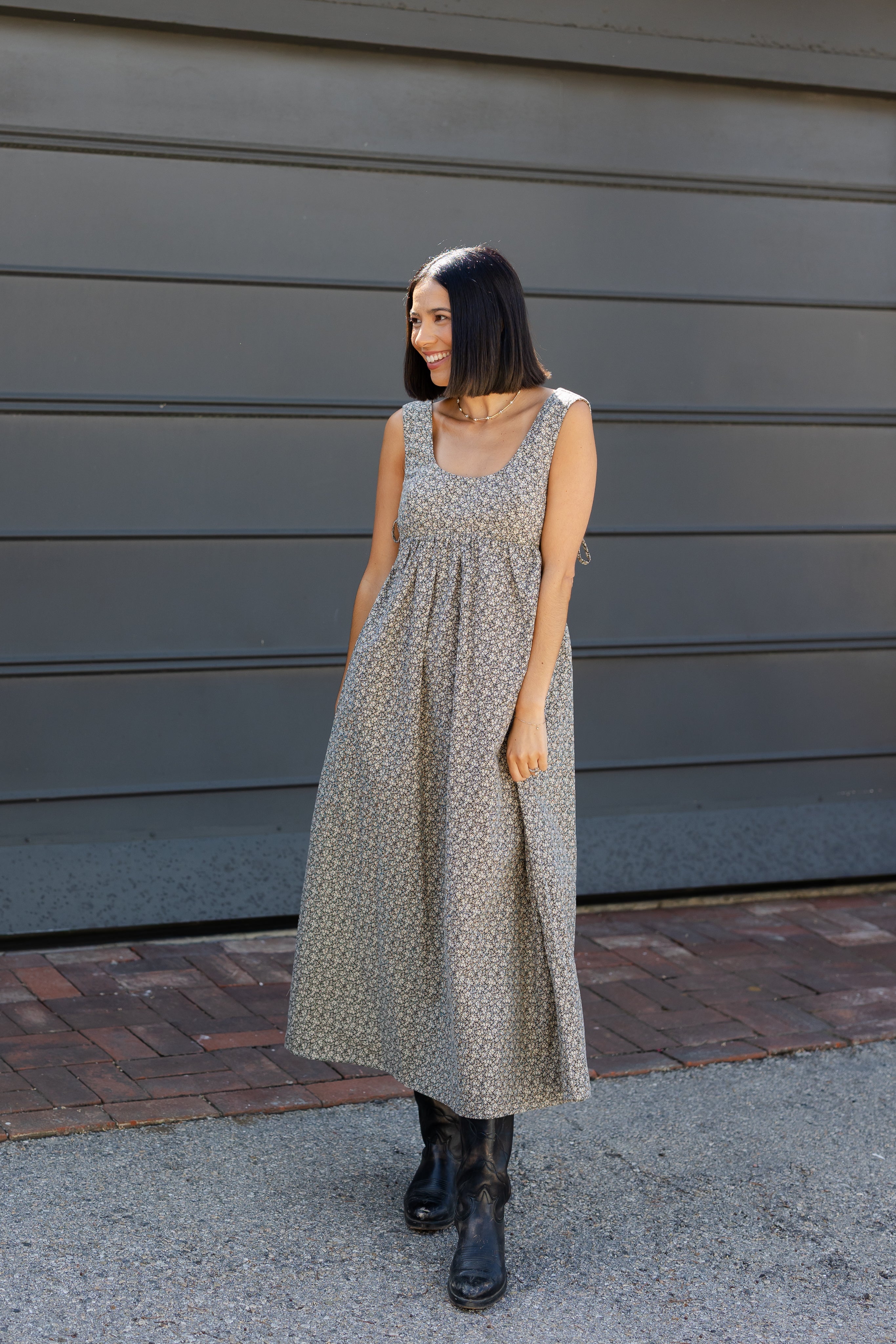 Woman in a patterned dress standing against a gray wall.