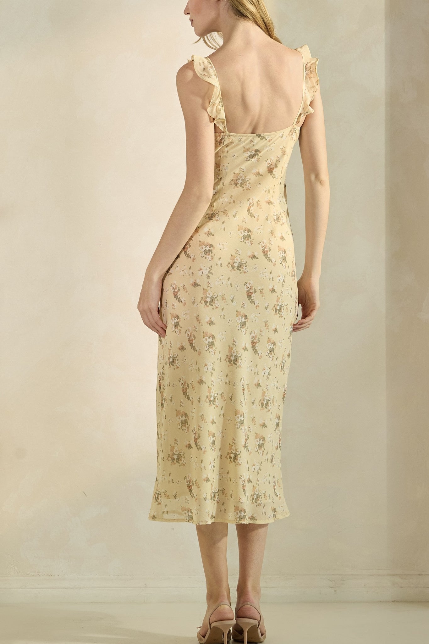 Woman wearing a light yellow floral dress against a neutral background