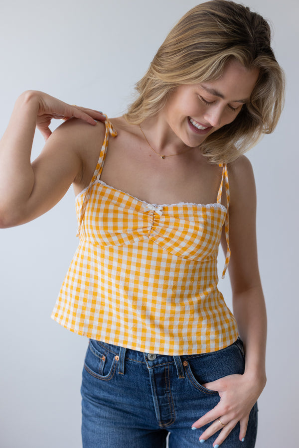 Woman wearing a yellow checkered top and blue jeans against a plain background