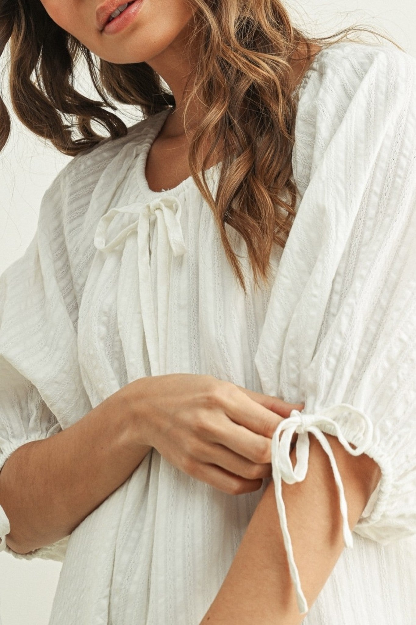 Woman wearing a white dress with a close-up of her hands adjusting the fabric.